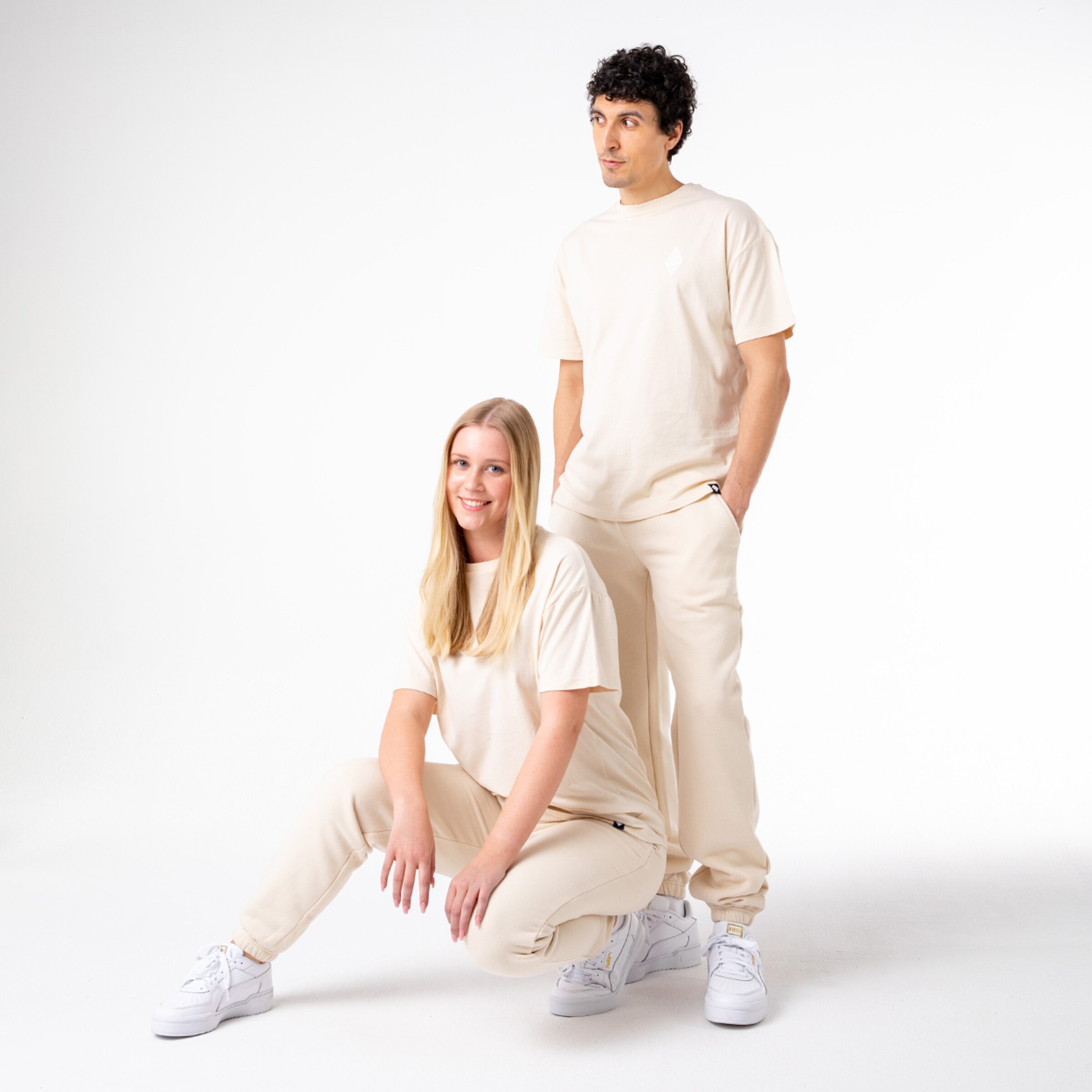 Zwei Personen in neutraler Kleidung eine kniet am Boden und die andere steht hinter ihr.