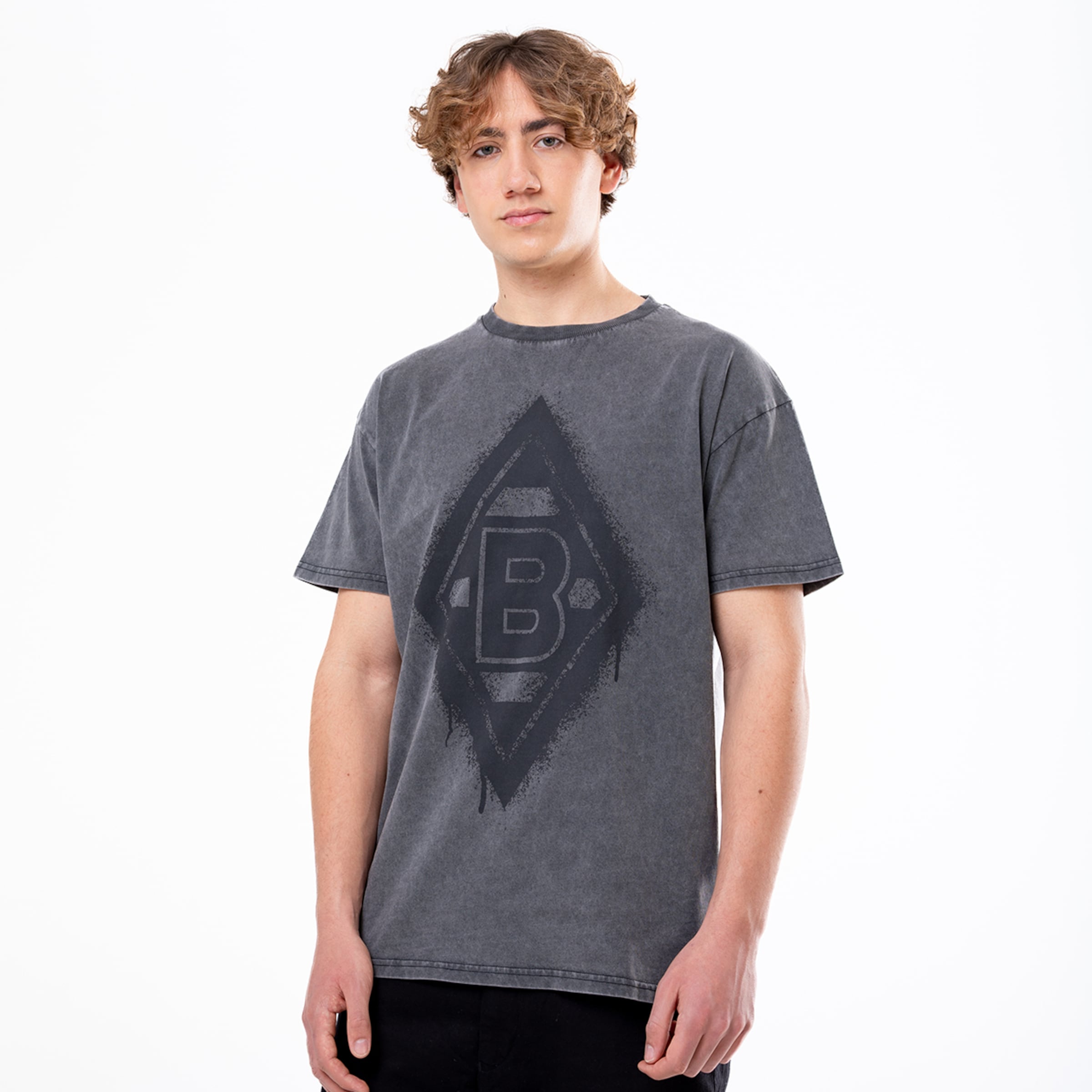 Junger Mann trägt ein graues T-Shirt mit einem großen dunklen B-Logo von Borussia Mönchengladbach.