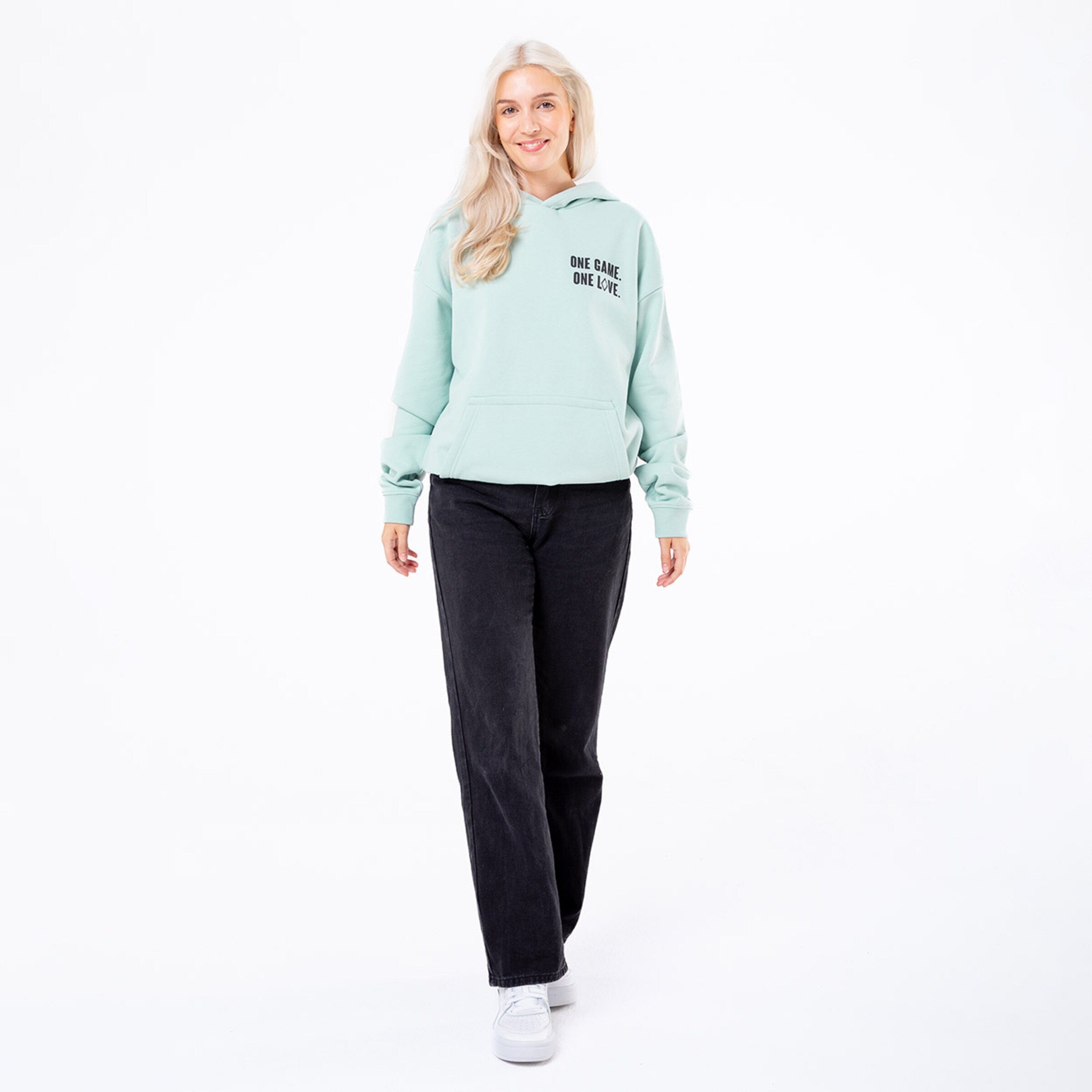 Junge Frau in mintgrüner Kapuzenjacke schwarze Hose lächelnd.