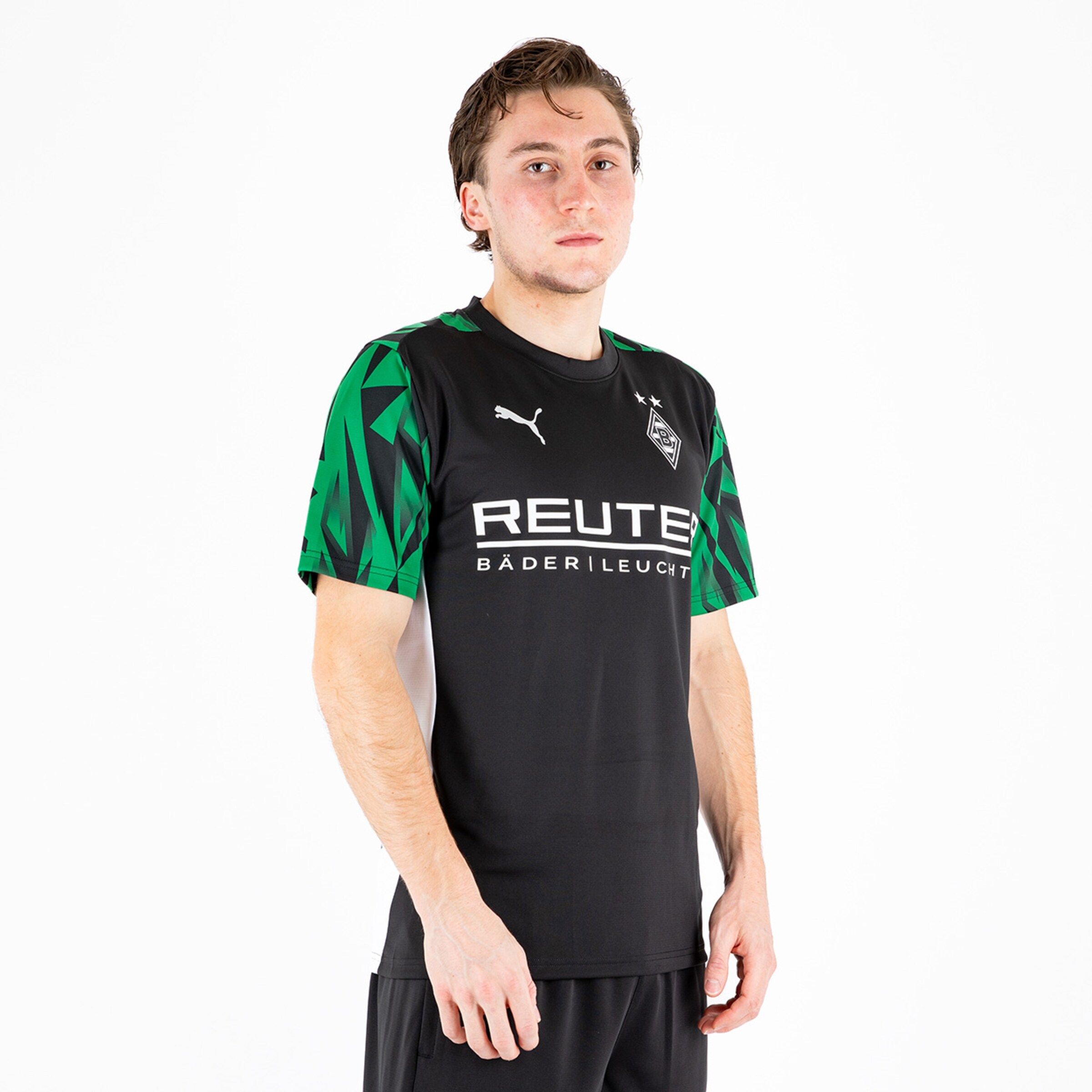 Ein junger Mann trägt ein schwarzes Fußballtrikot mit grünem Muster und Logo von Borussia Mönchengladbach.