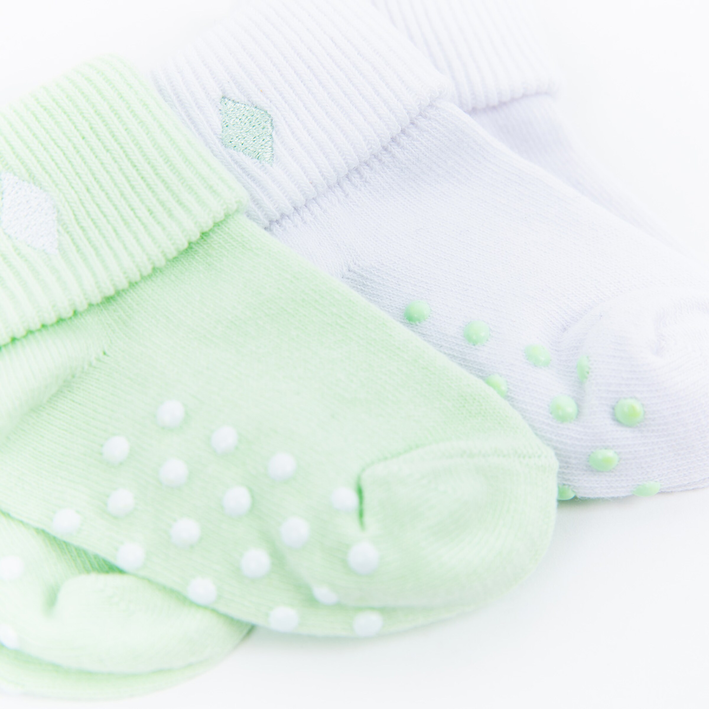 Zwei Paar Socken in hellgrün und weiß mit gepunkteten und diamondförmigen Designs.