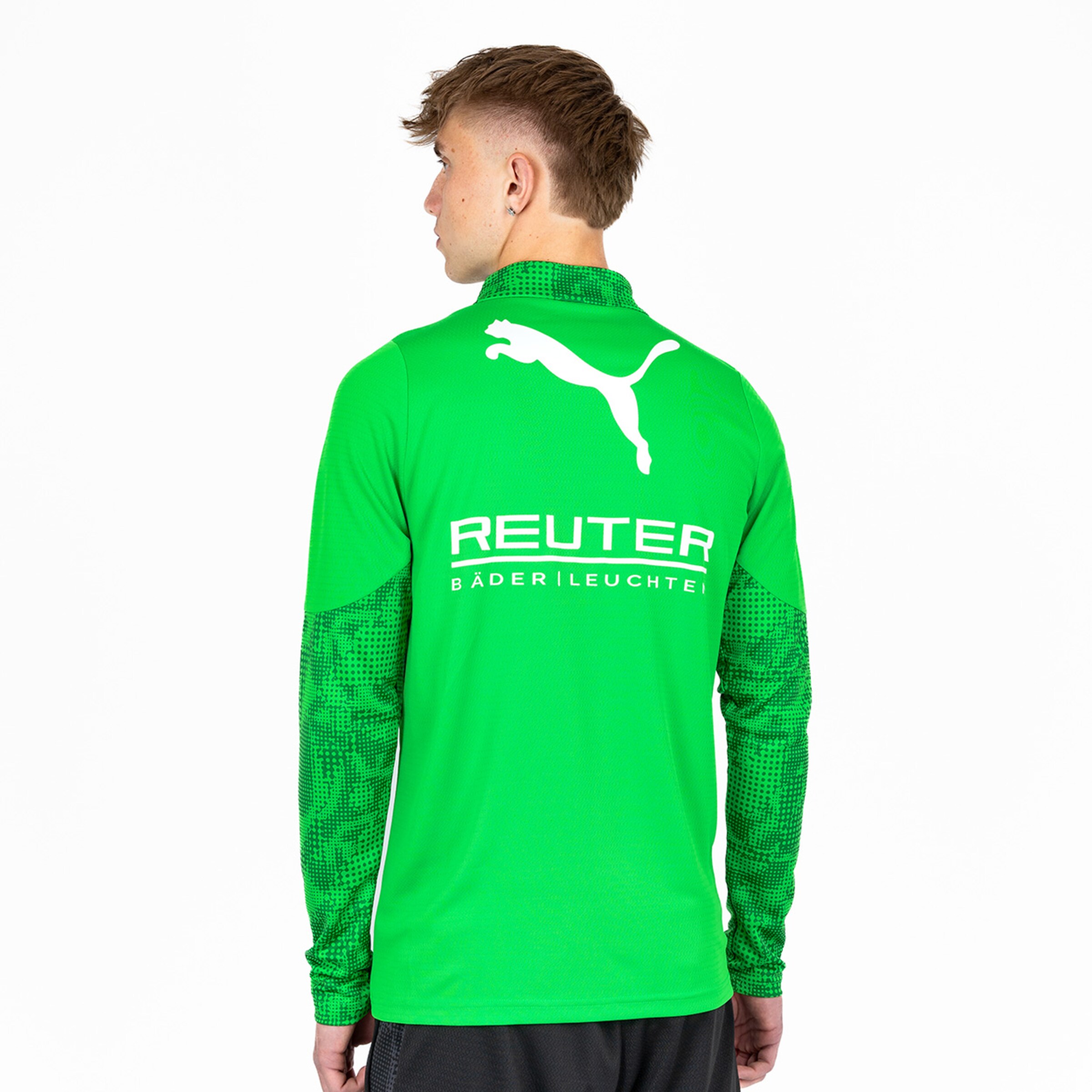 Ein junger Spieler trägt ein grünes Fußballtrikot mit langen Ärmeln und sieht von hinten aus.