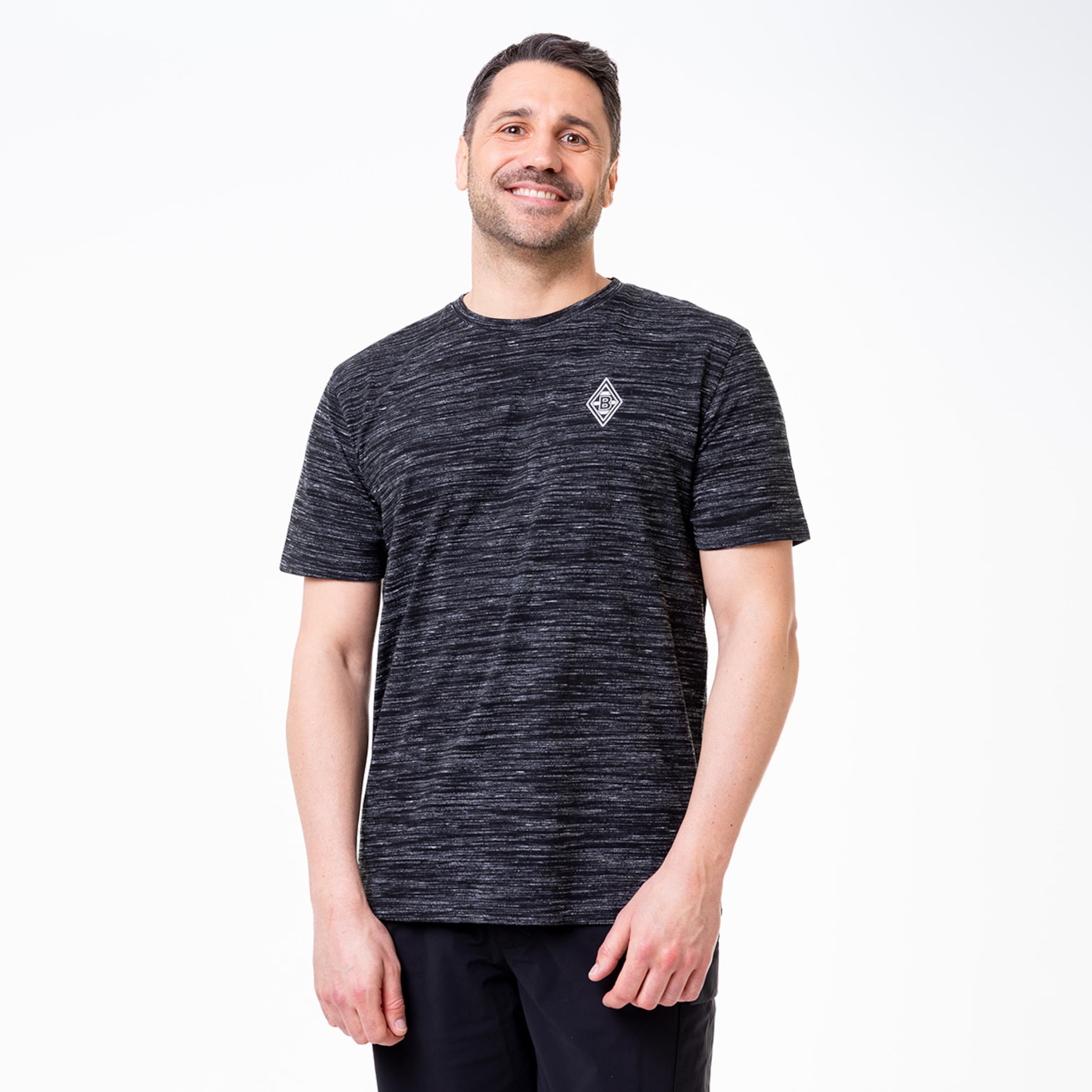 Mann in schwarzem gestreiftem T-Shirt mit Borussia Mönchengladbach Logo lächelnd.