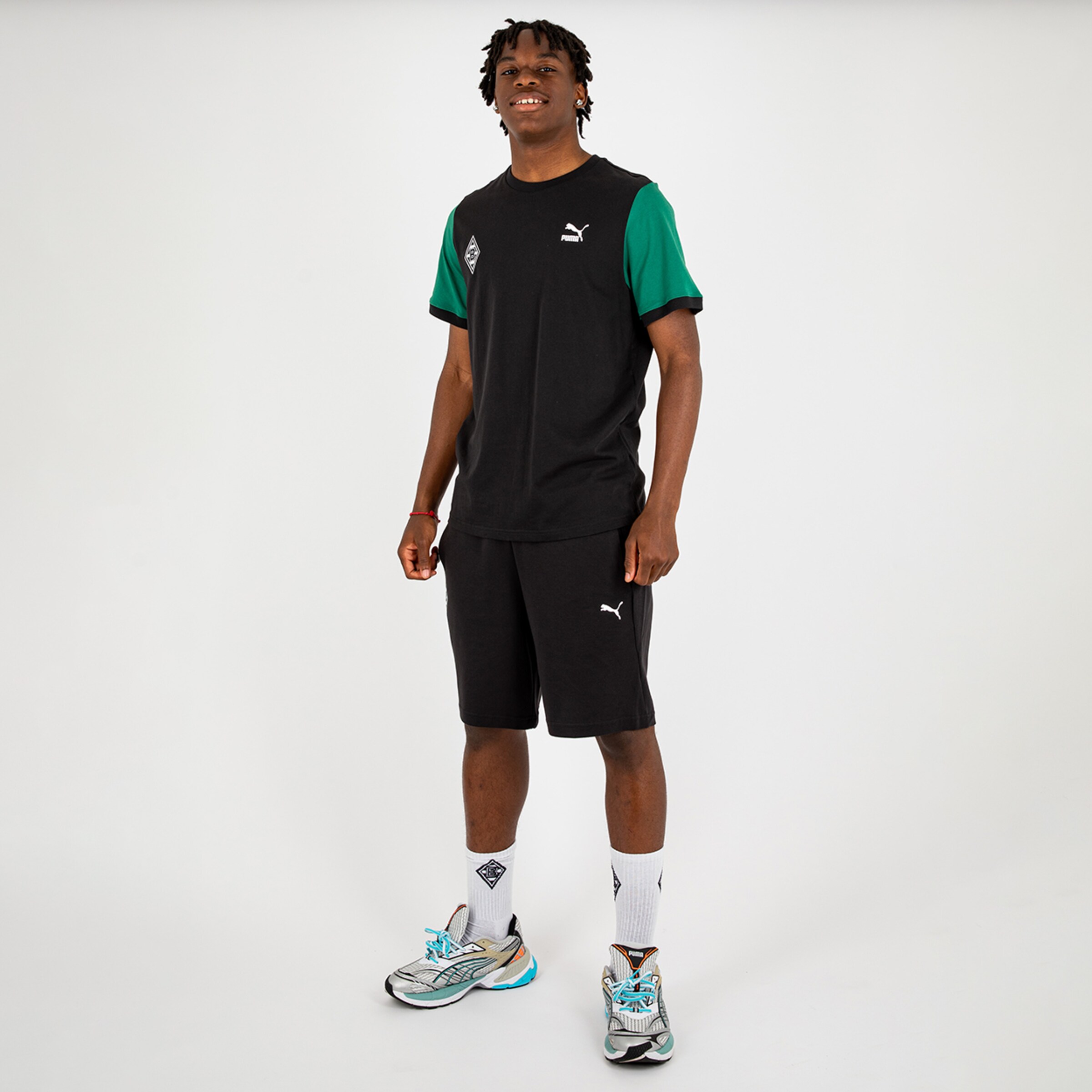 Player in black and green PUMA outfit wearing shorts and shoes posing against a neutral background.