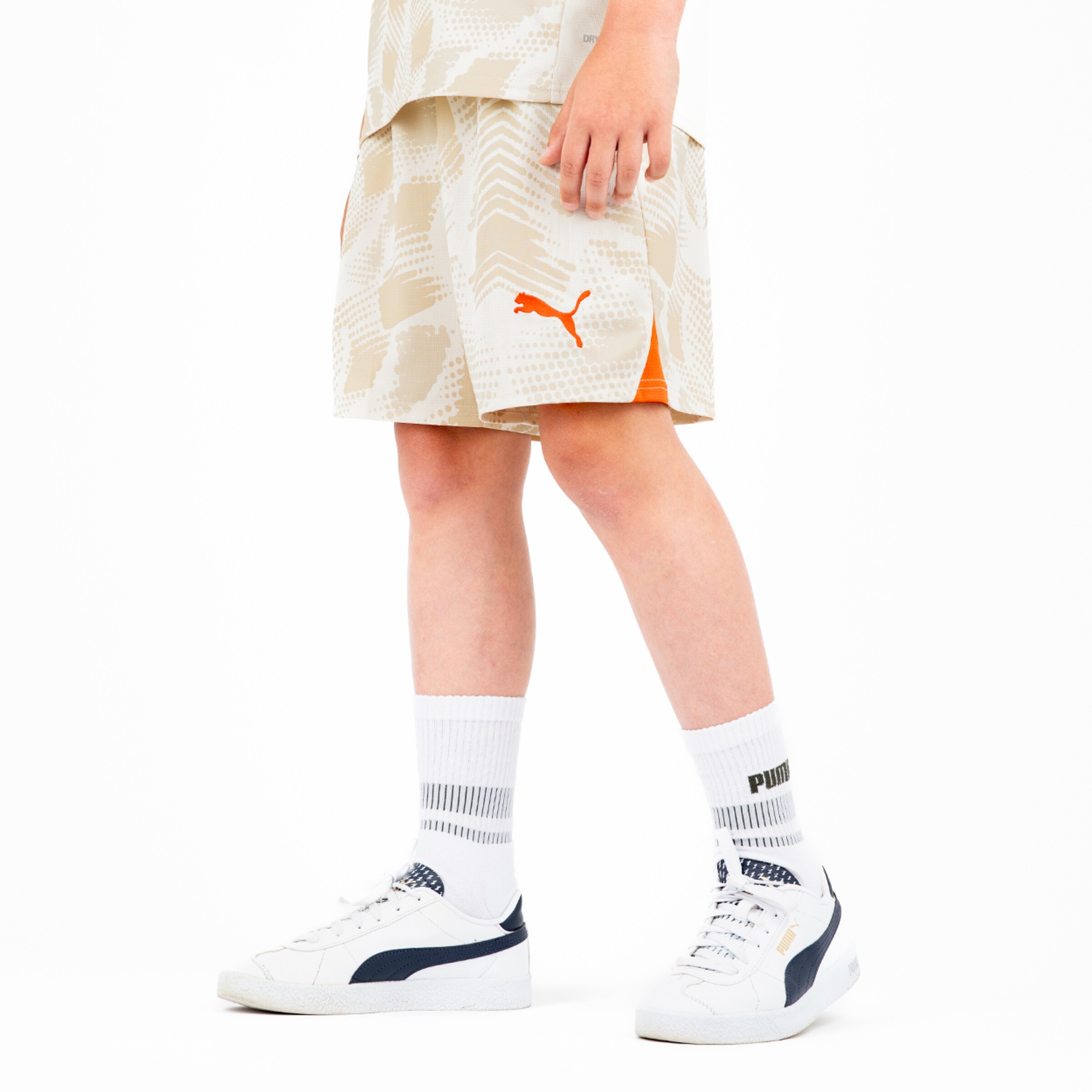Boy wearing light football shorts by Puma with orange logo white socks and shoes.
