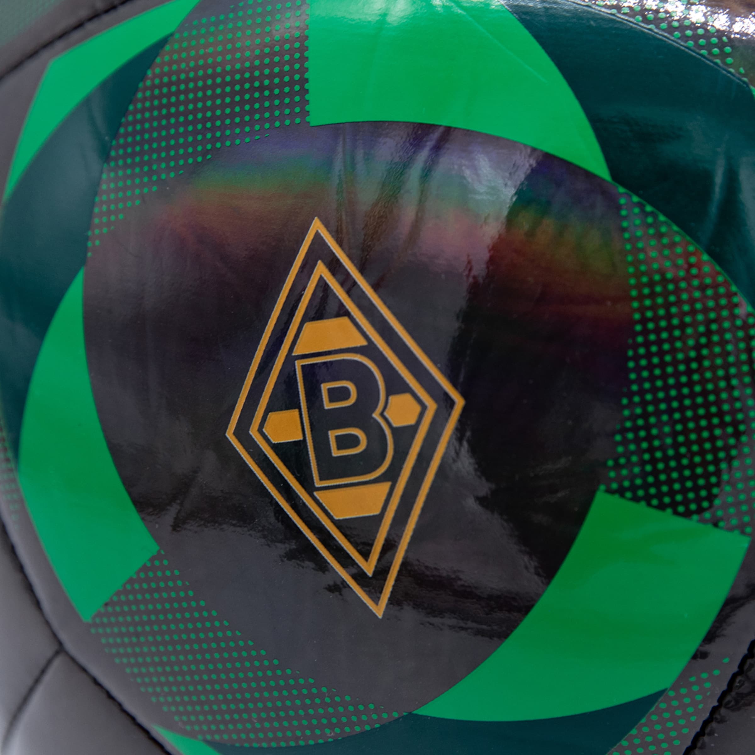 Nahaufnahme des Borussia Mönchengladbach Logos auf einem grün-schwarzen Fußball mit glänzender, irisierender Oberfläche.
