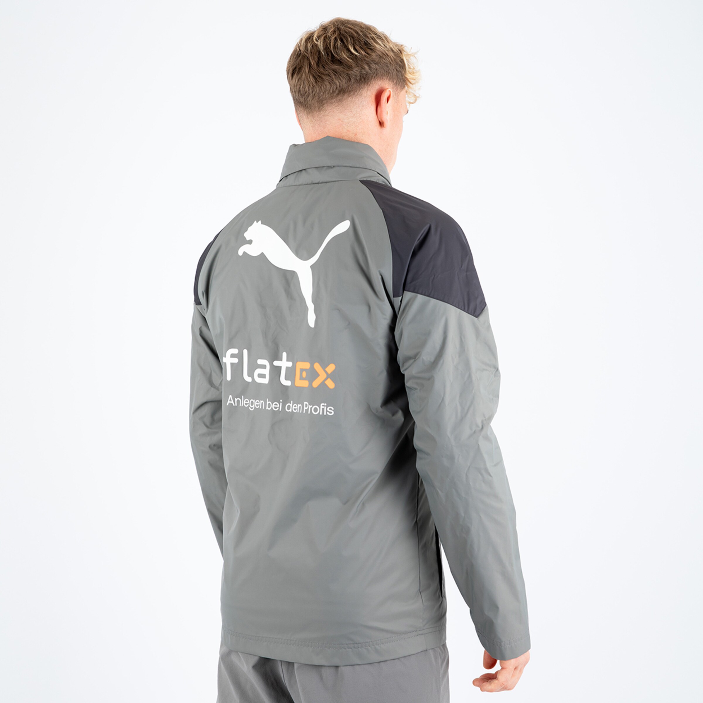 Mann trägt graue Jacke von Puma mit Logo hinten und Sponsorenaufdruck flatex.