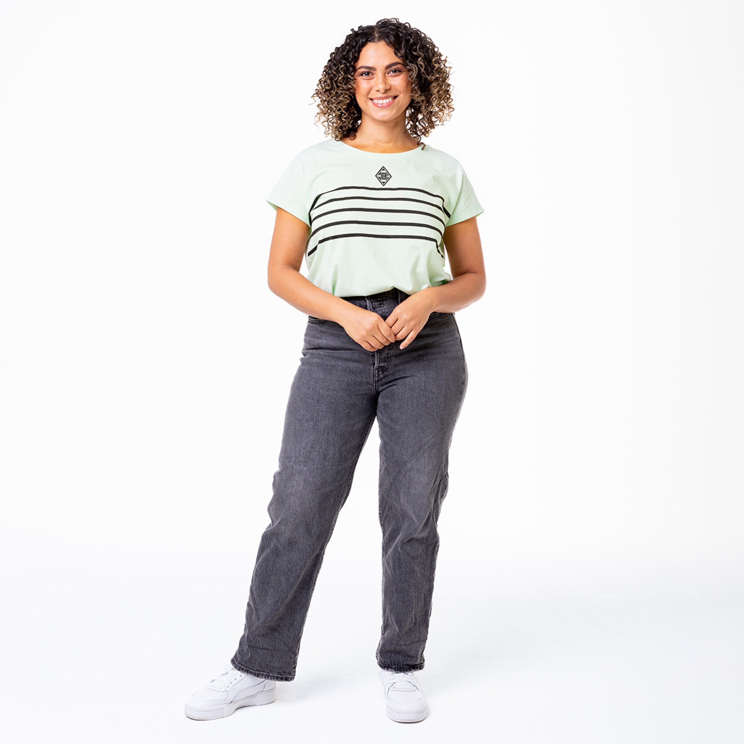 A woman with curly hair wearing a mint green striped t-shirt and black jeans.