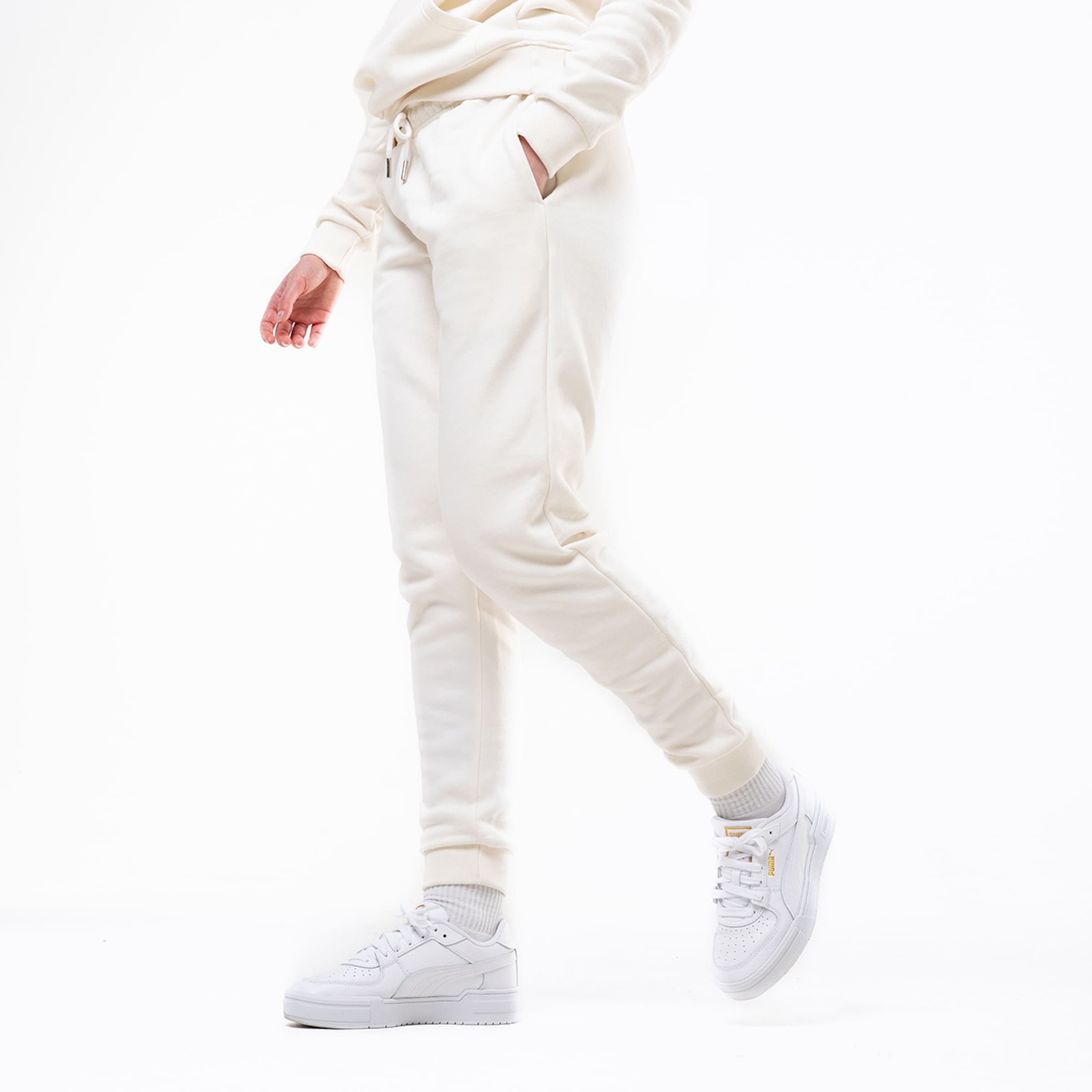 Beige Jogginghose mit Taschen und weißen Sneakers in einem neutralen Raum.