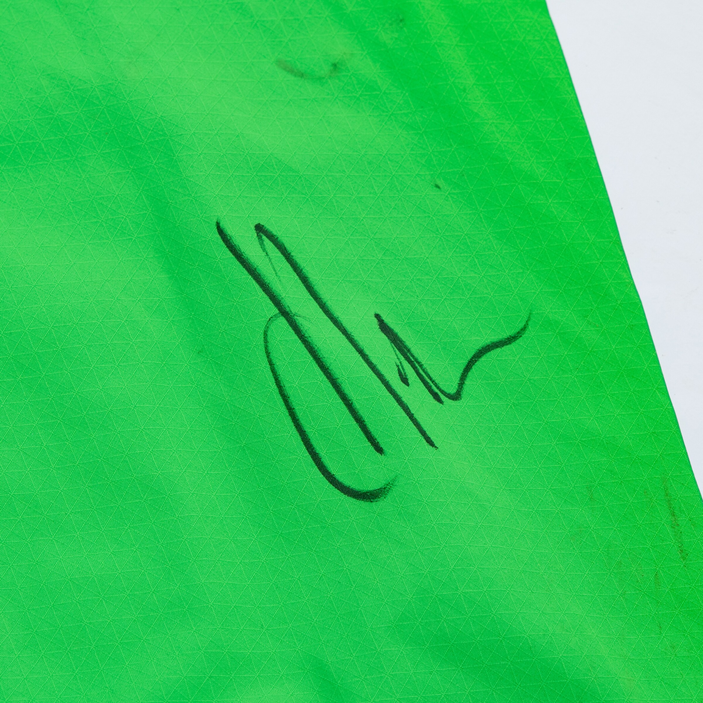 Close-up of neon green diamond-textured fabric featuring a flowing black signature.