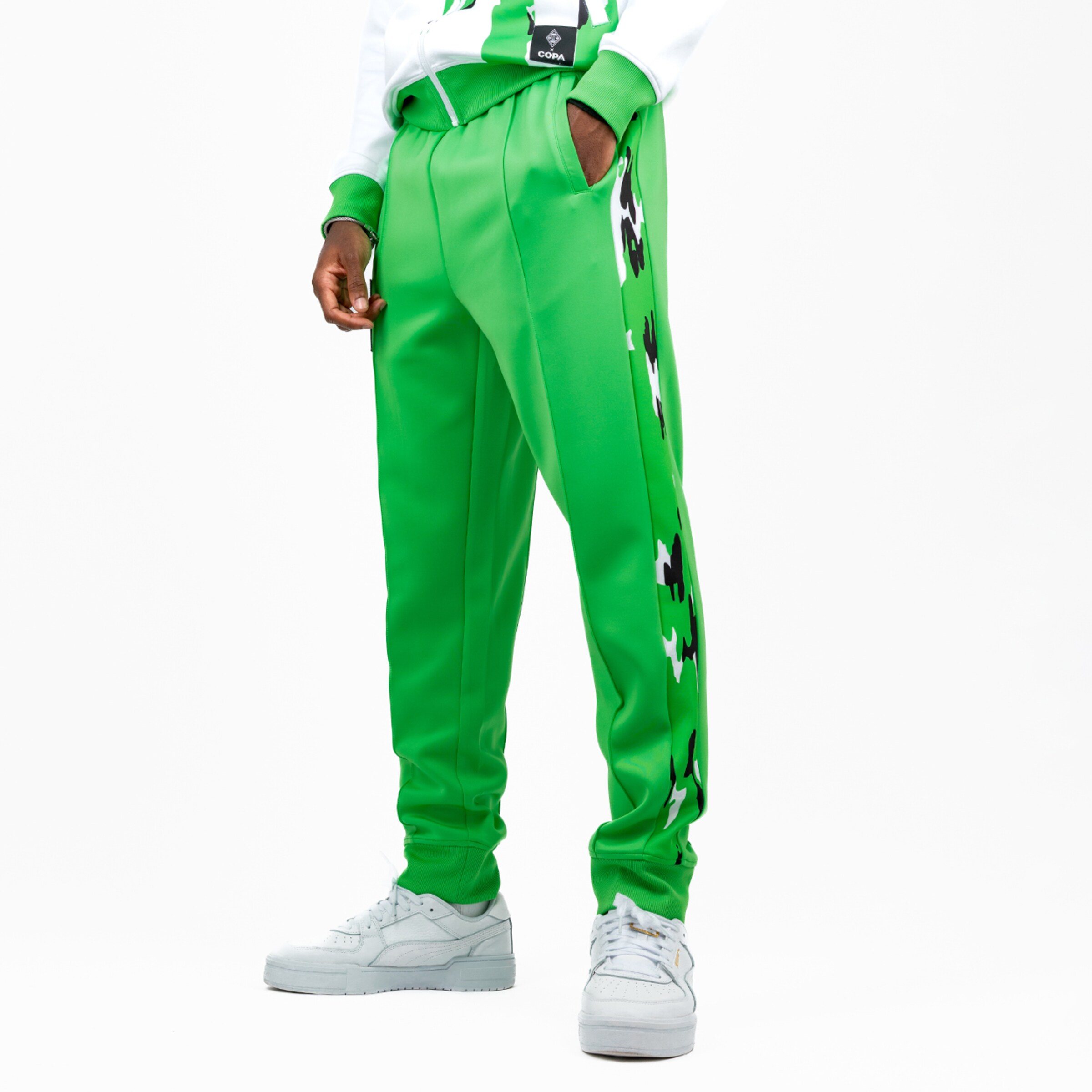 Grüne Sporthose mit seitlichem Muster kombiniert mit weißen Sneakern.