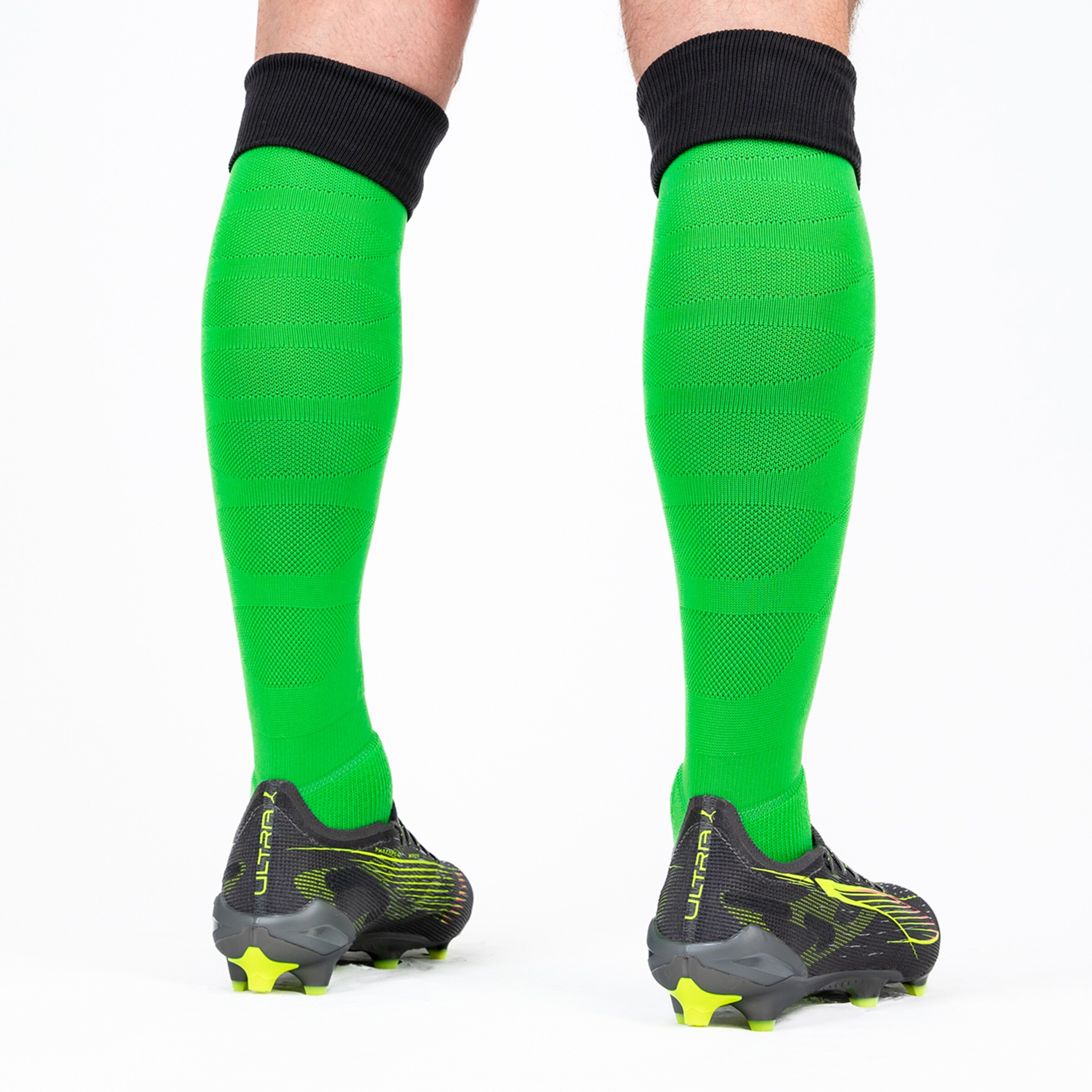 Green football socks with black cuff and football boots in the background.