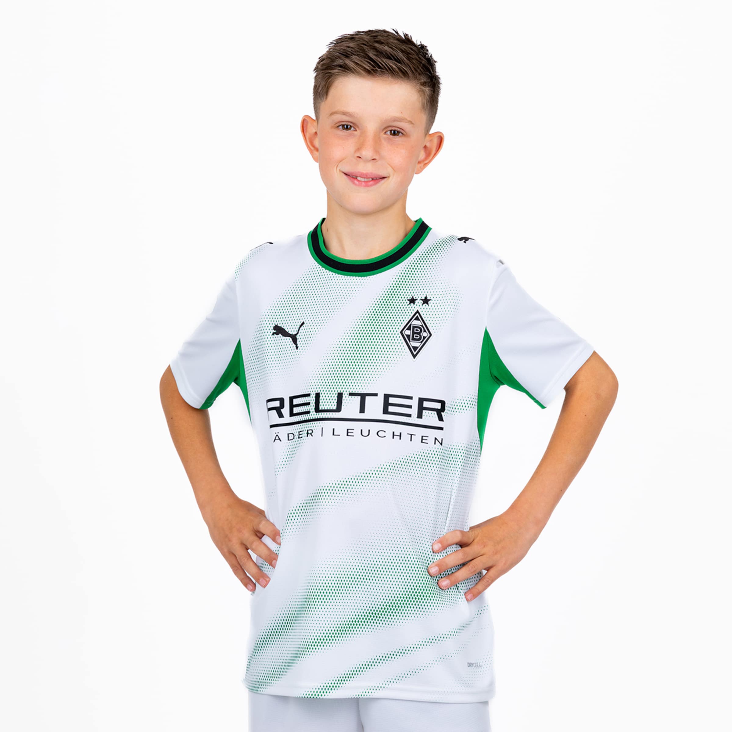 Lächelnder Junge im weiß-grünen Borussia Mönchengladbach Trikot mit REUTER-Sponsor, Hände in die Hüften gestützt, weißer Hintergrund.