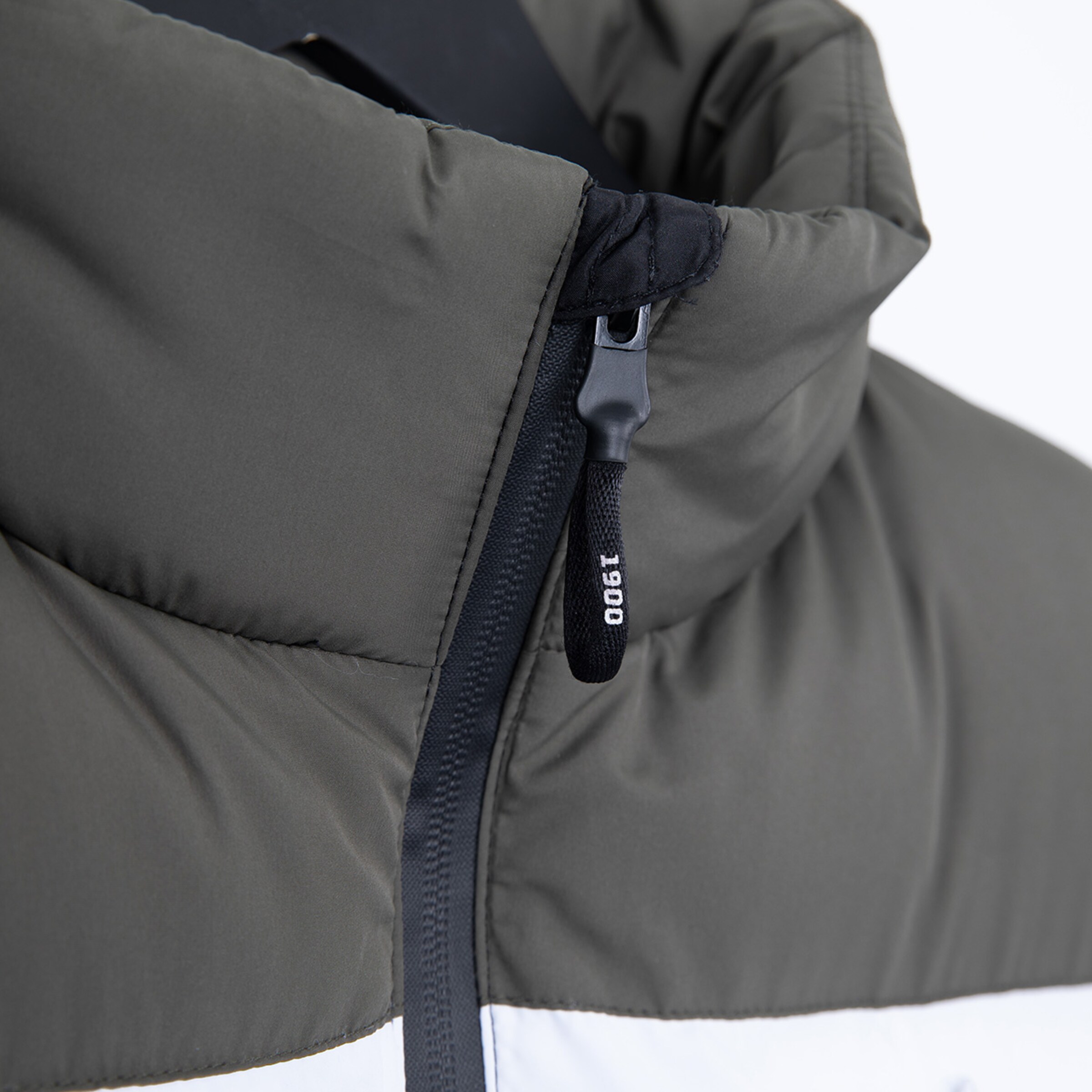 Nahaufnahme des Reißverschlusses einer grauen Jacke mit schwarzem Kragen und weißen Details.