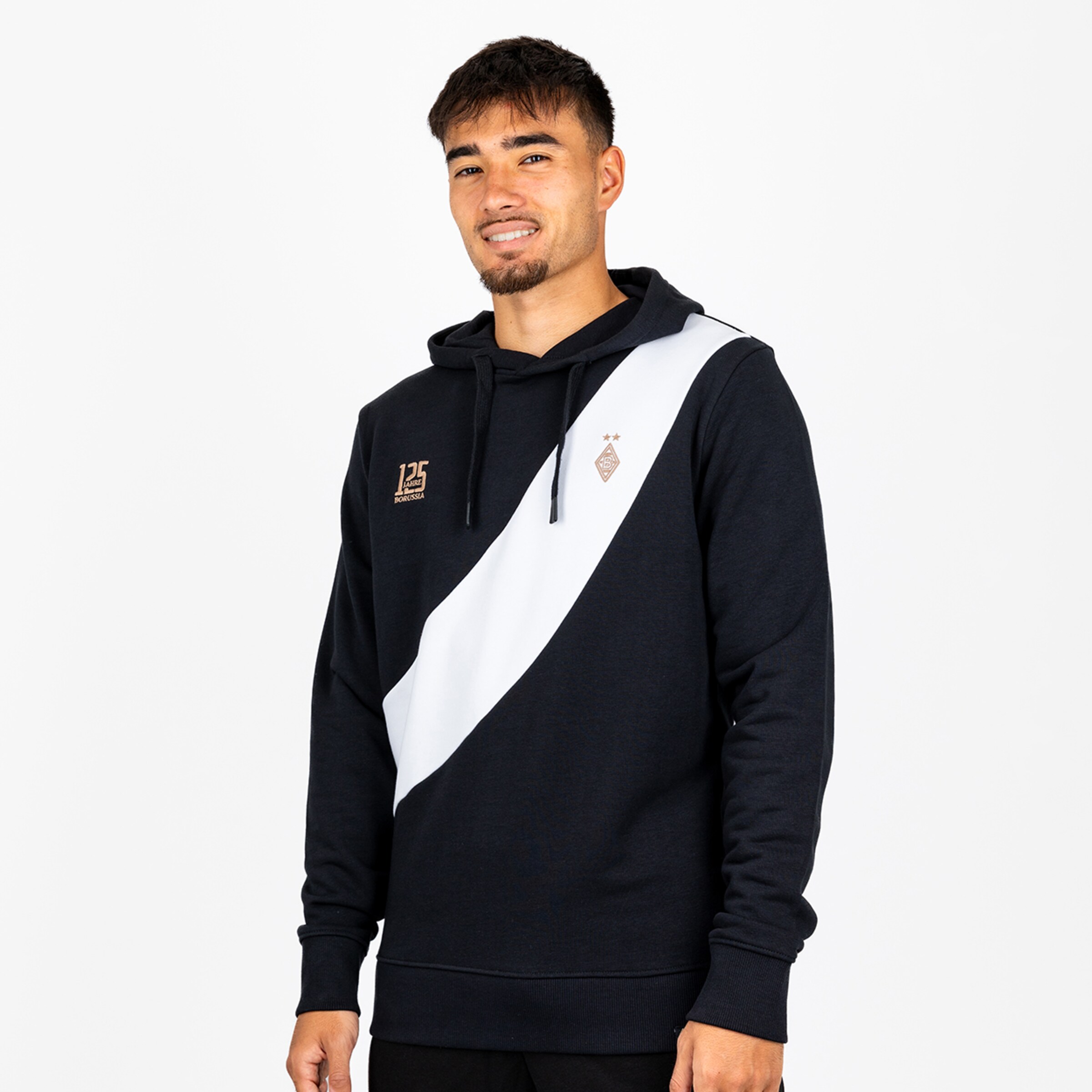 Mann in schwarzem 125 Jahre Borussia Hoodie mit weißem Schrägstreifen vor weißem Hintergrund.
