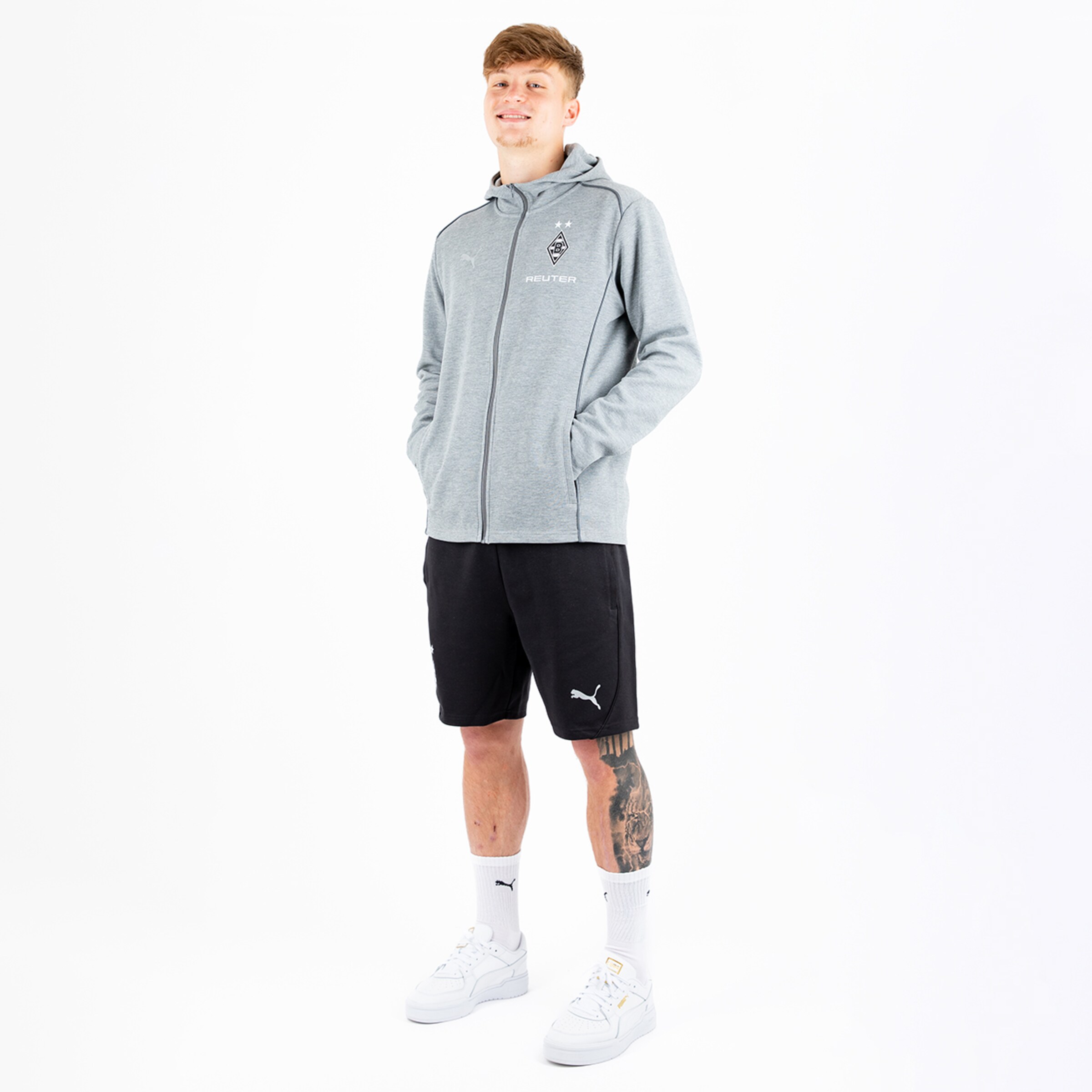 Ein junger Mann steht in Sportbekleidung aus Grau und Schwarz.