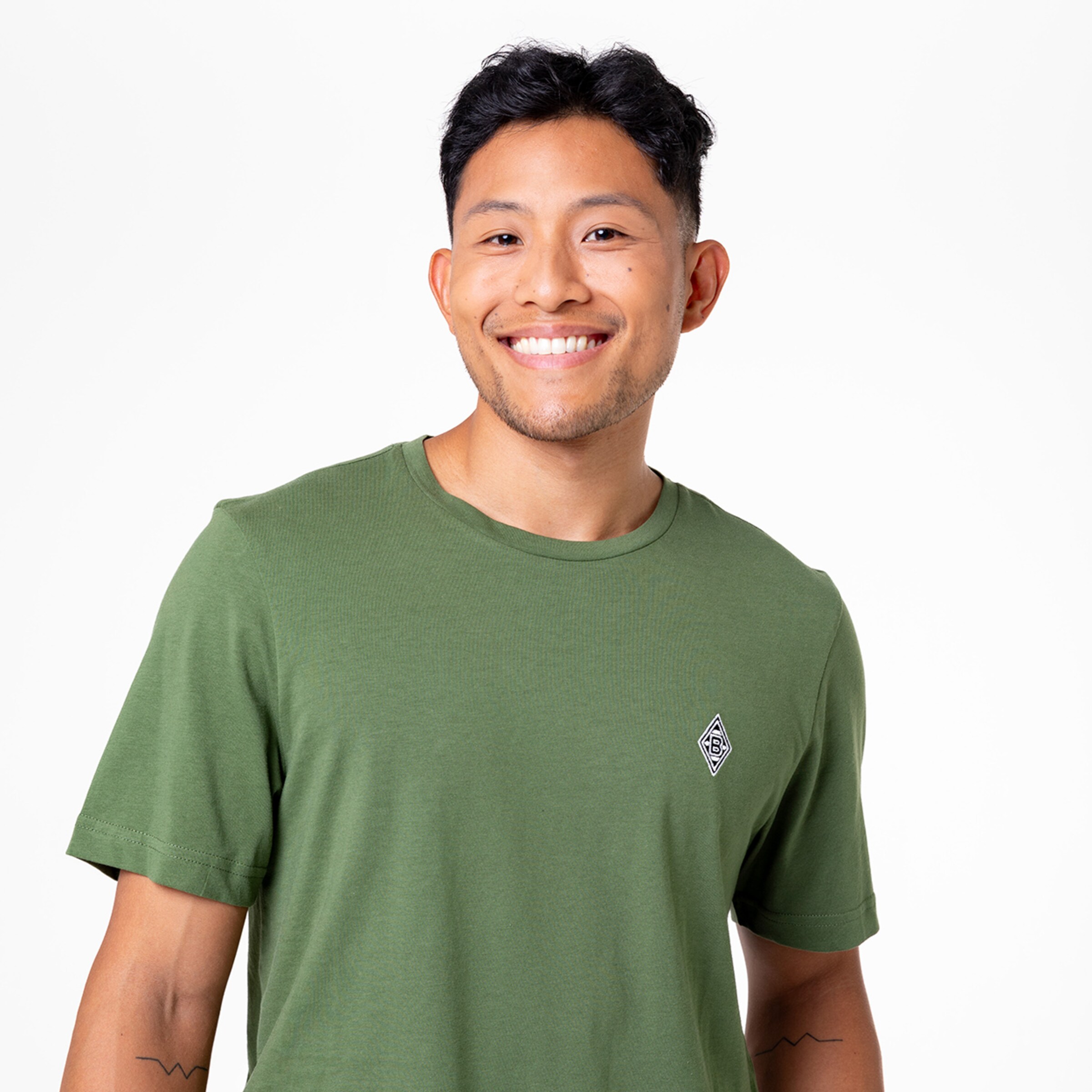 Lächelnder junger Mann mit kurzer Frisur in einem grünen T-Shirt mit Stickerei.