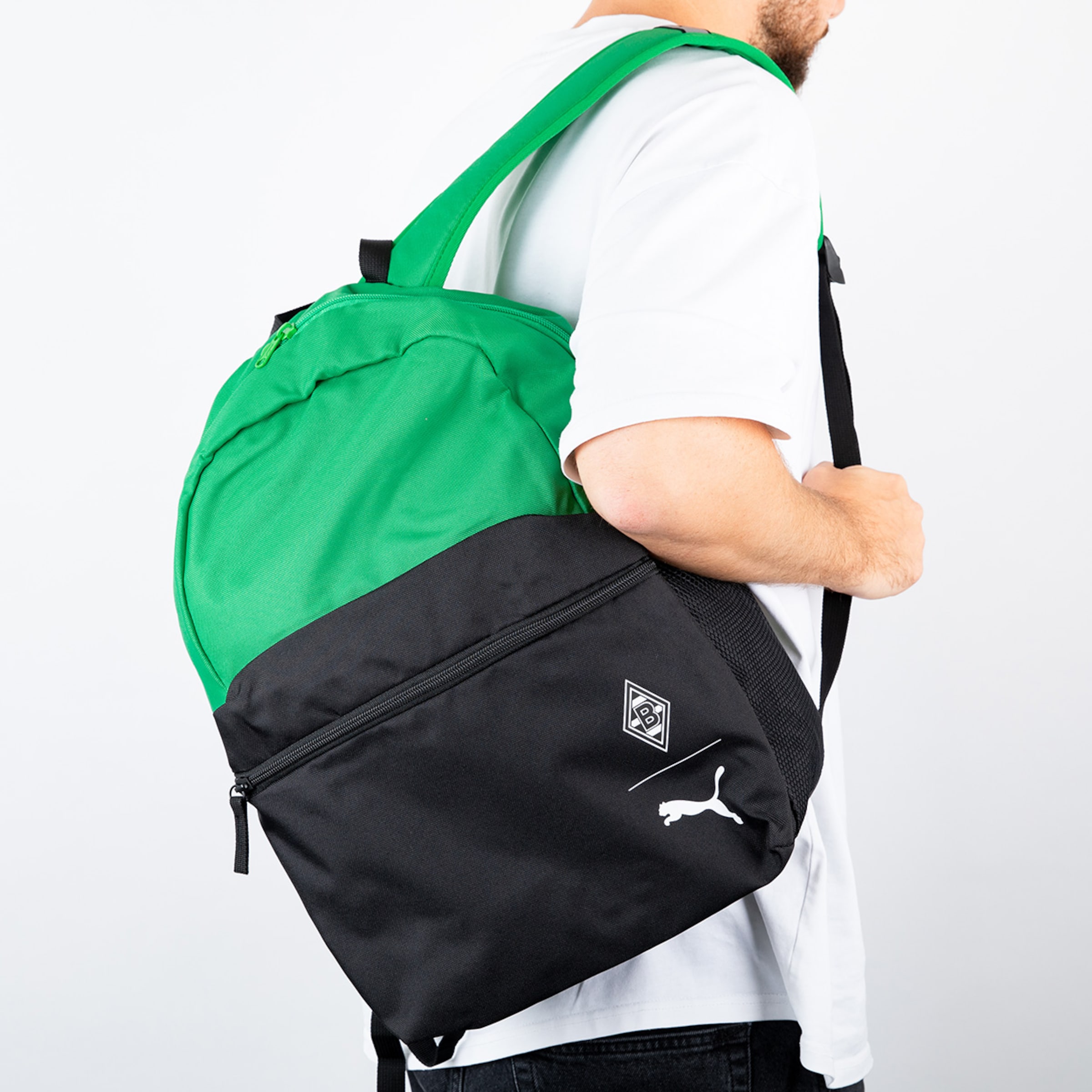 Schwarzer und grüner Rucksack von Puma getragen von einer Person vor neutralem Hintergrund.