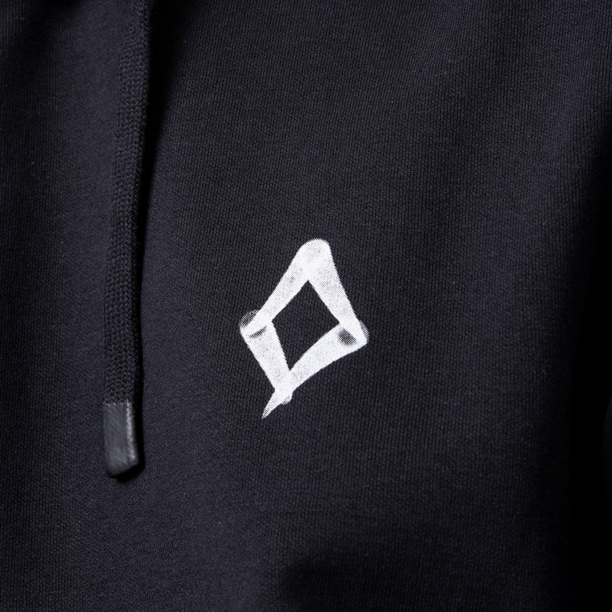 Nahaufnahme eines schwarzen Hoodies mit einem weißen, handgemalten quadratischen Logo und einer schwarzen Kordel.