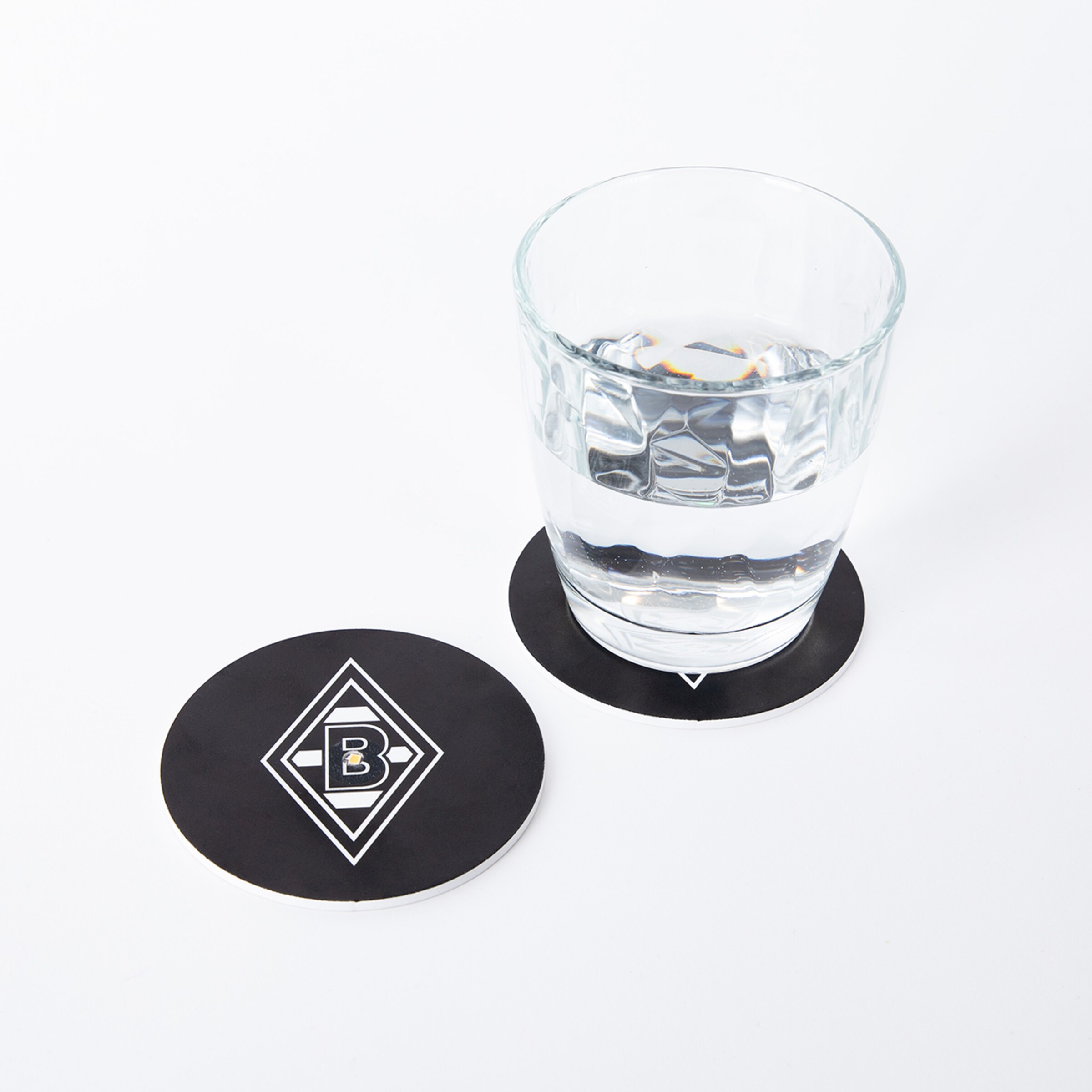 Ein schwarzer Untersetzer mit dem Borussia Mönchengladbach-Logo unter einem Glas Wasser.