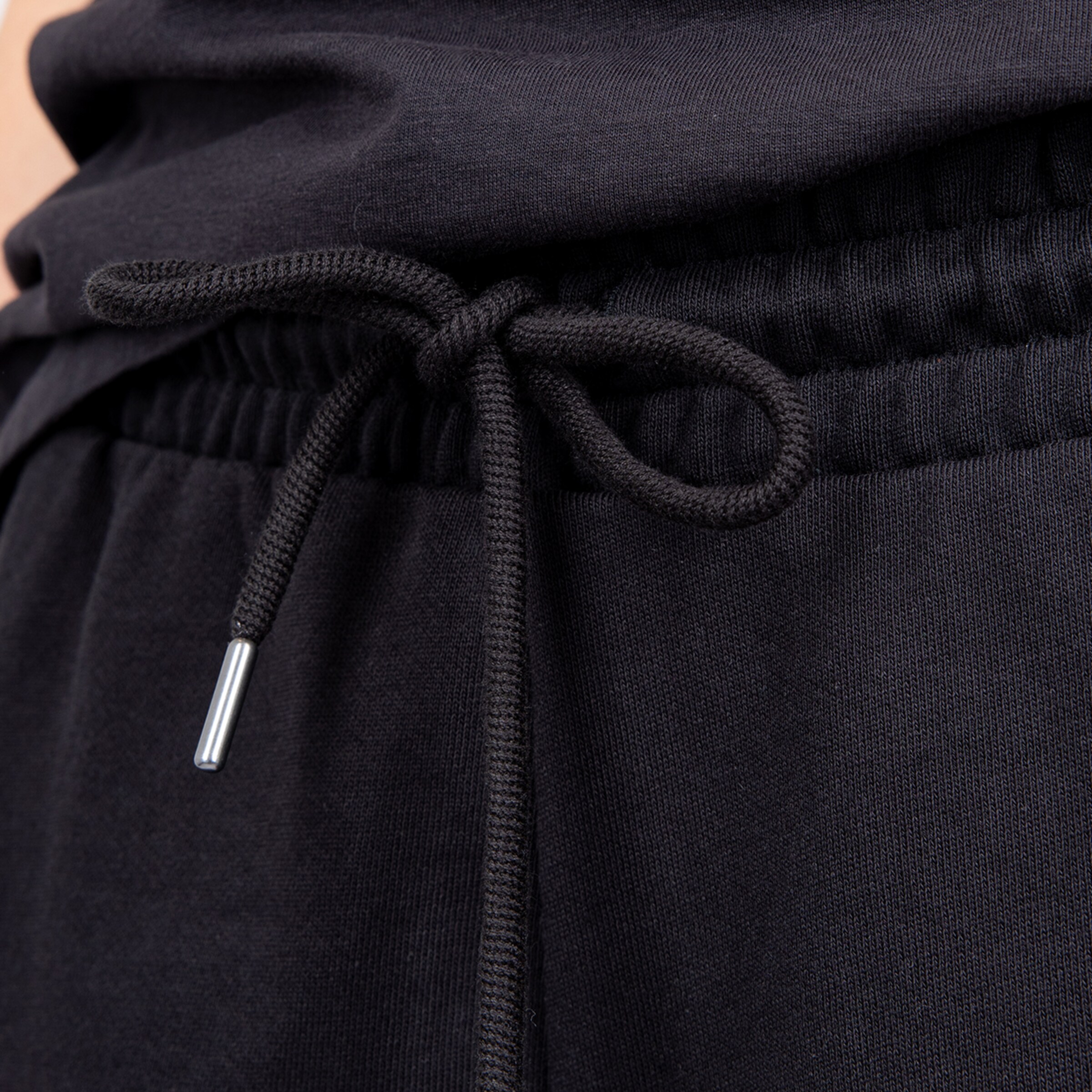Nahaufnahme einer schwarzen Jogginghose mit elastischem Bund und Kordelzug mit silberner Metallspitze.