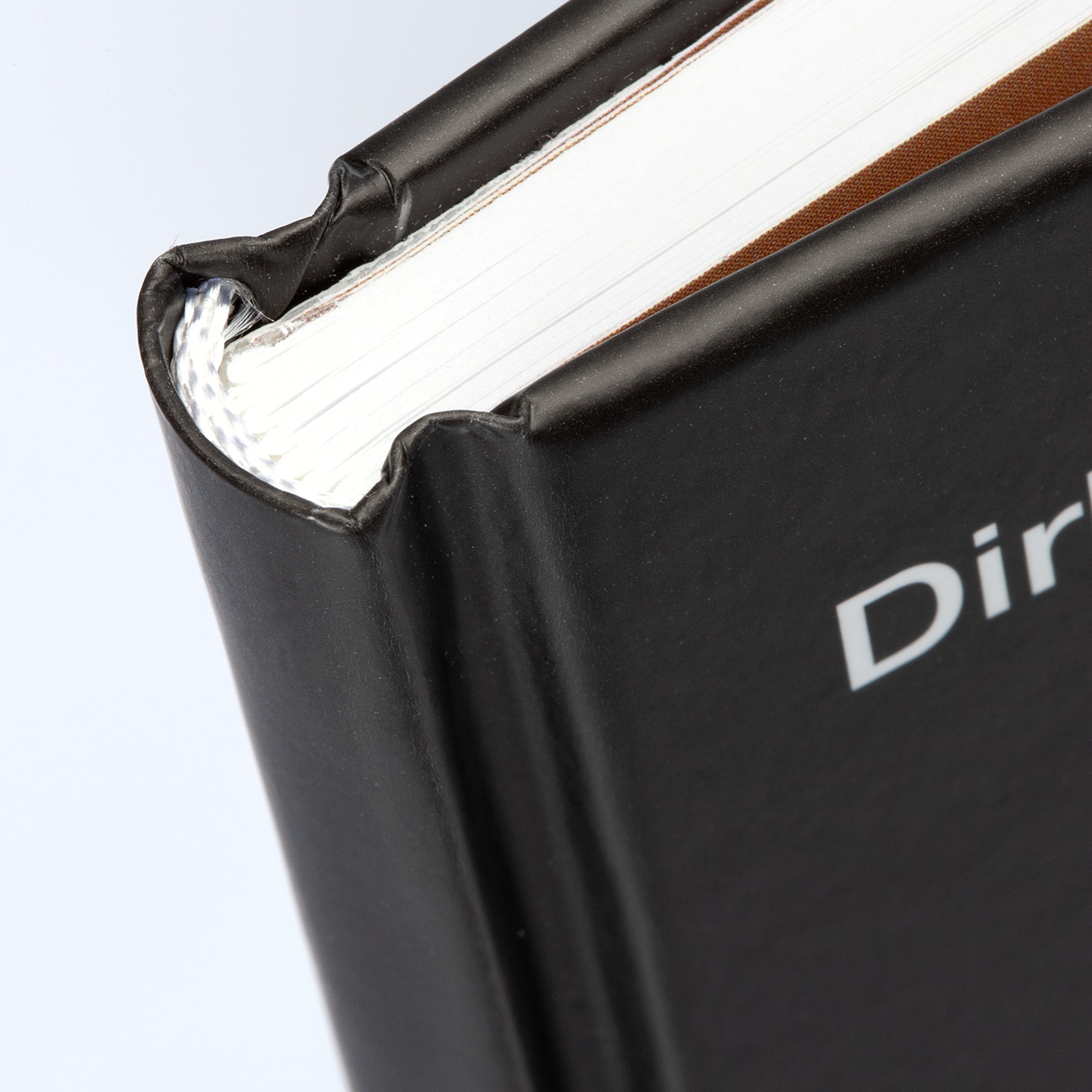Nahaufnahme der Bindung eines schwarzen Hardcover-Buchs mit weißen Seiten, gestreiftem Kapitalband und dem Textanfang „Dir“.