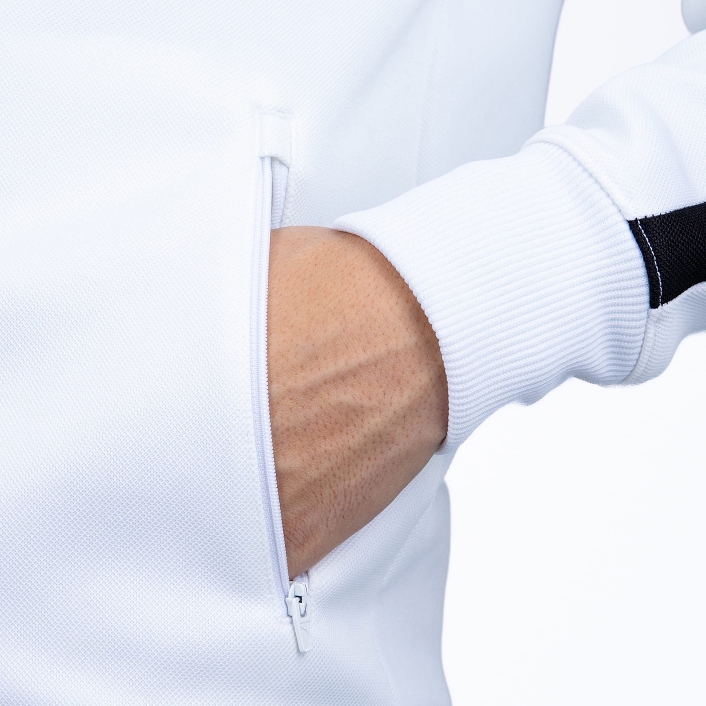 Nahaufnahme einer Hand in der Reißverschlusstasche einer weißen Sportjacke mit gerippten Ärmelbündchen.