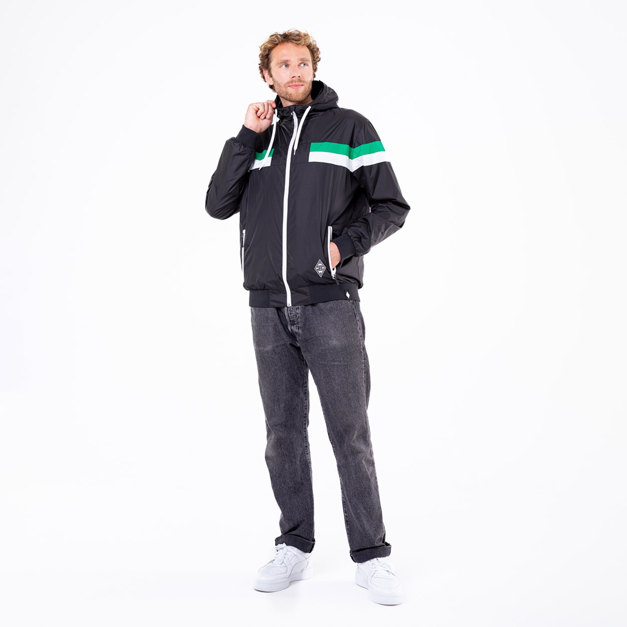 Mann in sportlicher Jacke mit Kapuze und gestreiftem Design trägt Jeans und Sneakers.