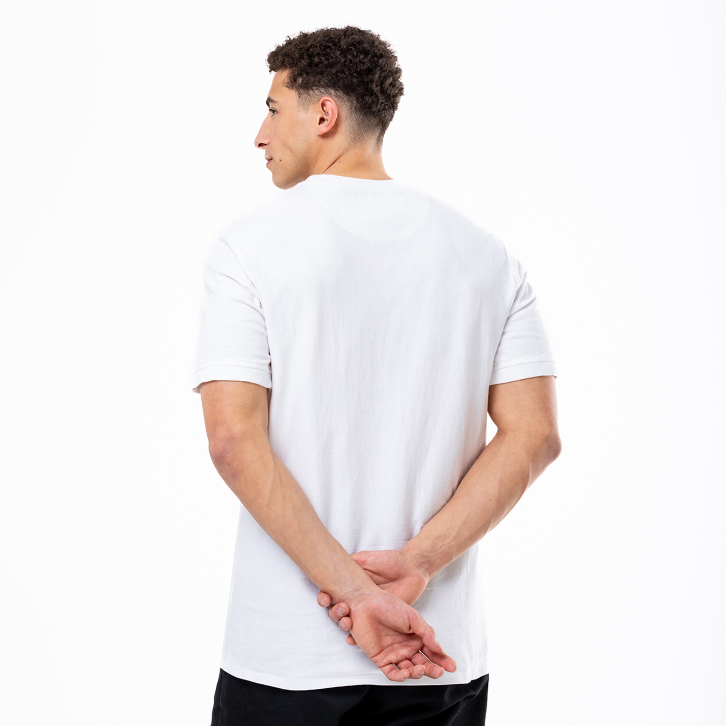 Mann mit lockigem Haar in einem weißen T-Shirt Rückenansicht Hände hinter dem Rücken verschränkt.