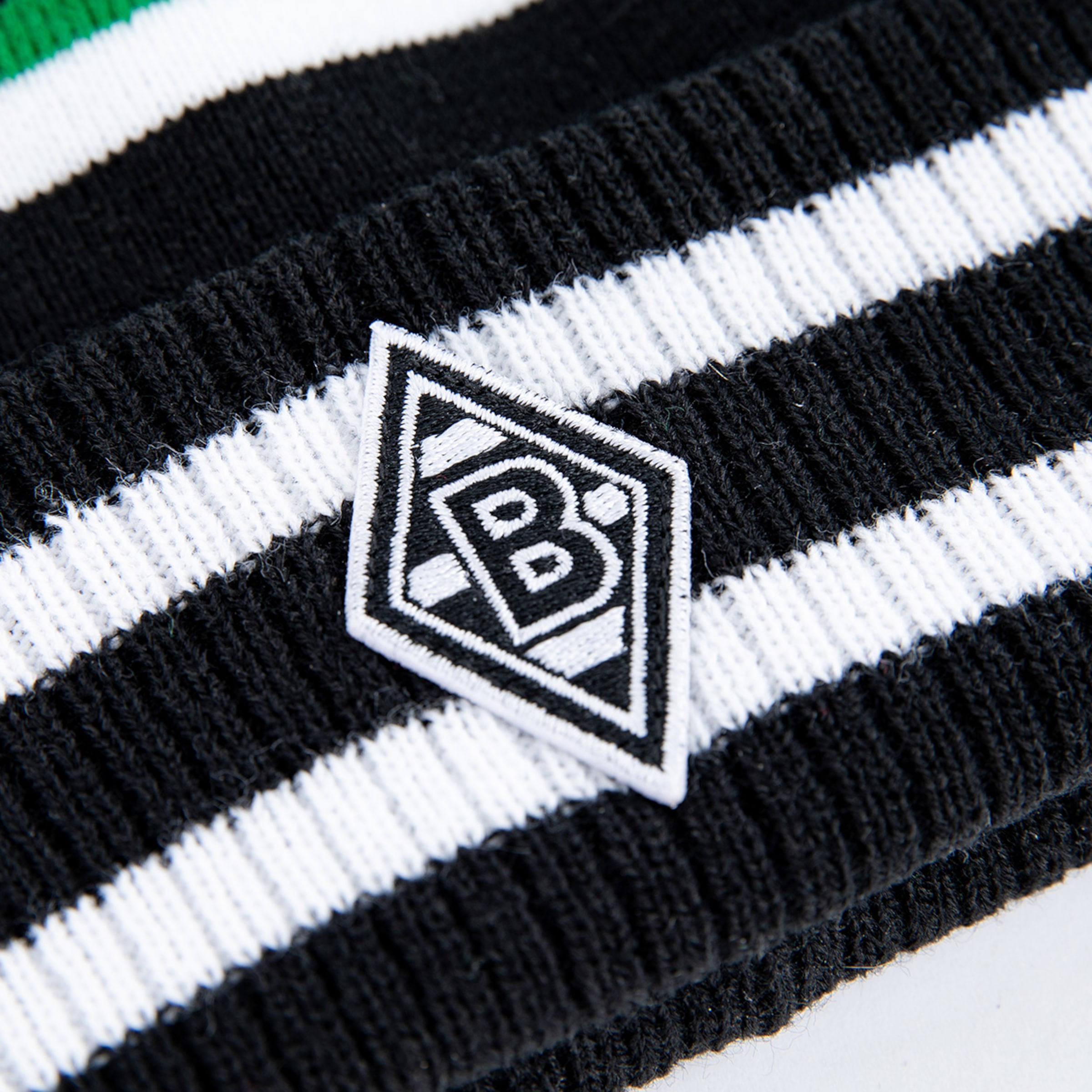 Nahaufnahme eines schwarz-weiß gestreiften Strickstoffes mit dem aufgestickten Rauten-Logo von Borussia Mönchengladbach.