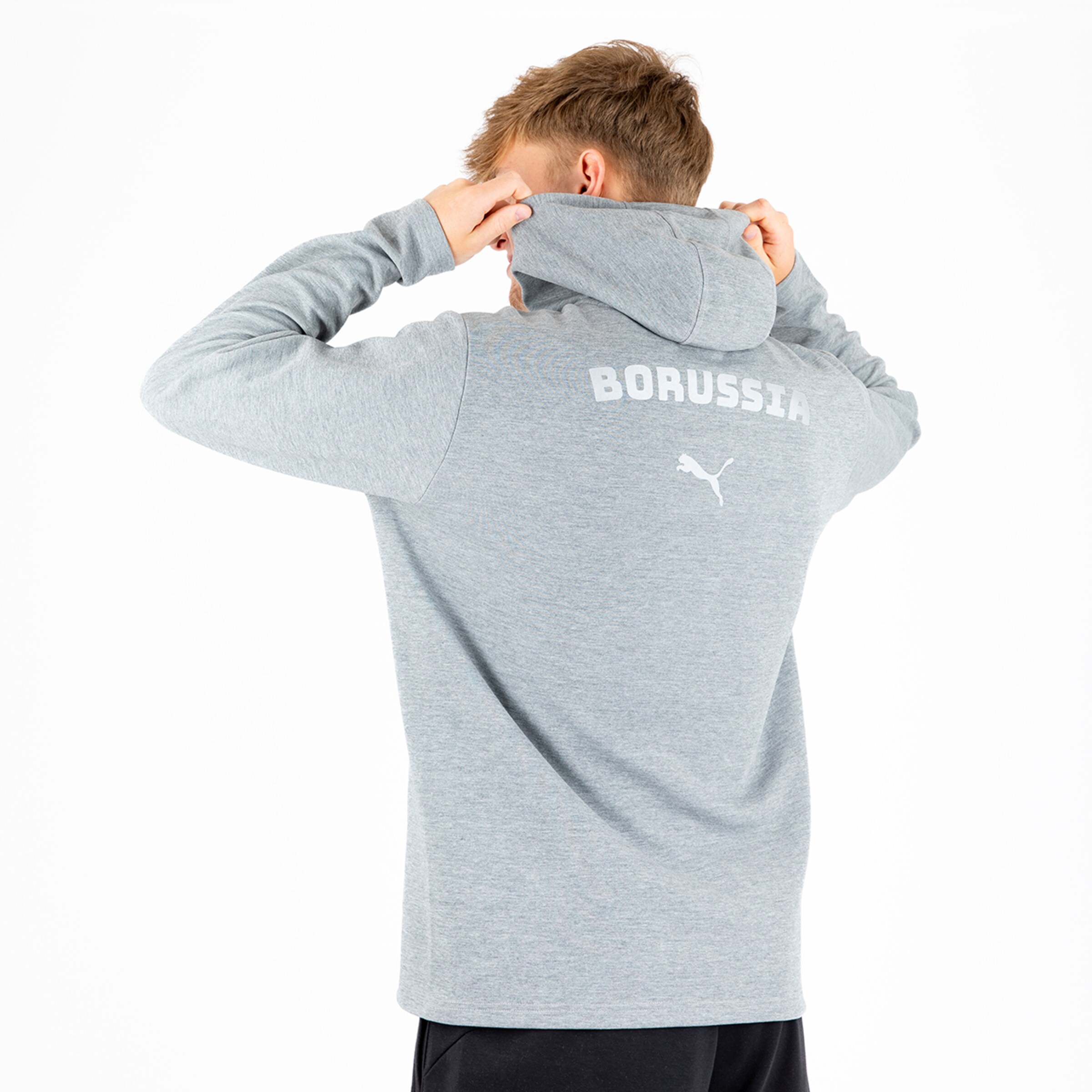 Ein junger Mann trägt einen grauen Kapuzenpullover mit dem Aufdruck BORUSSIA auf dem Rücken.