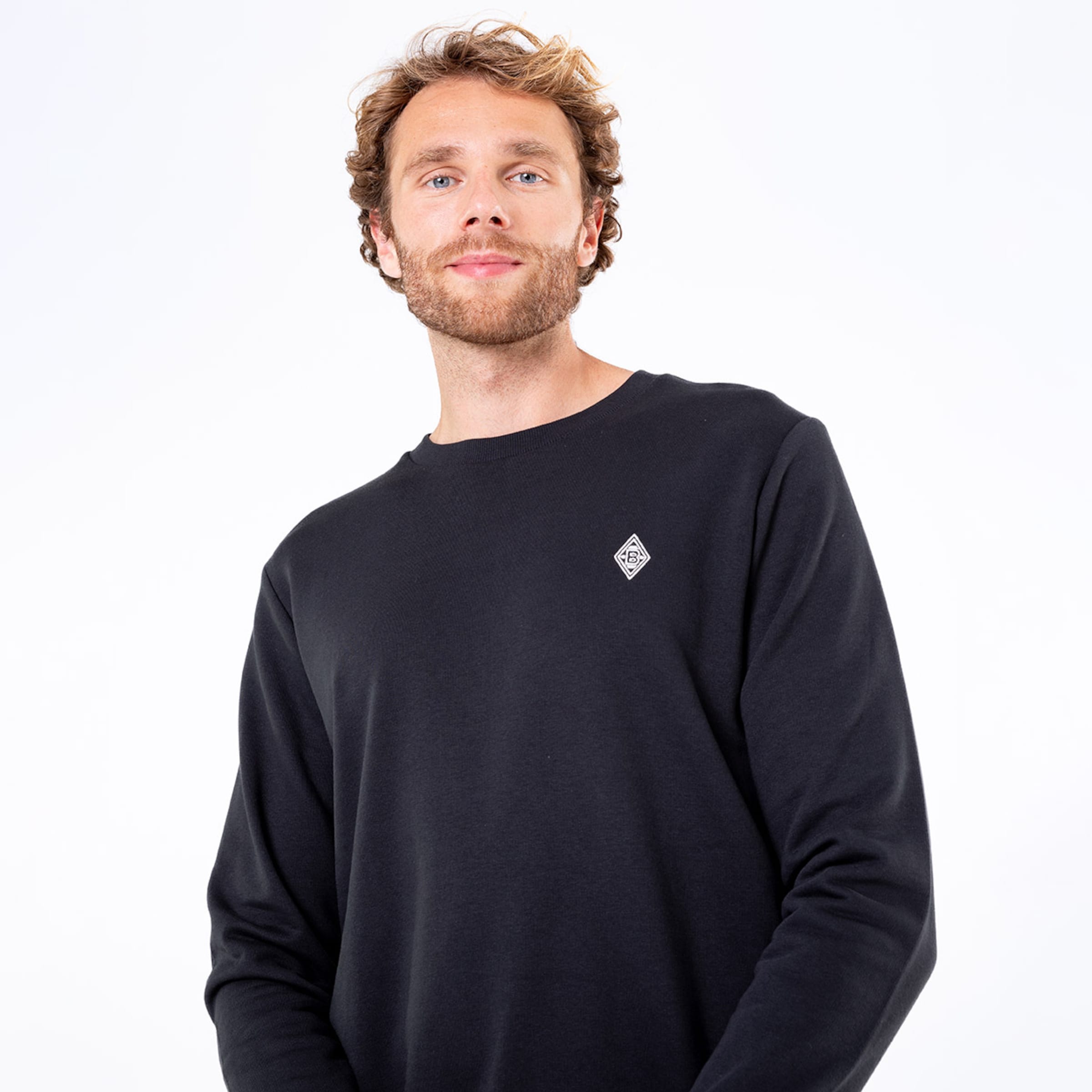 Mann trägt einen schwarzen Pullover mit einem dezenten Logo auf der Brust.