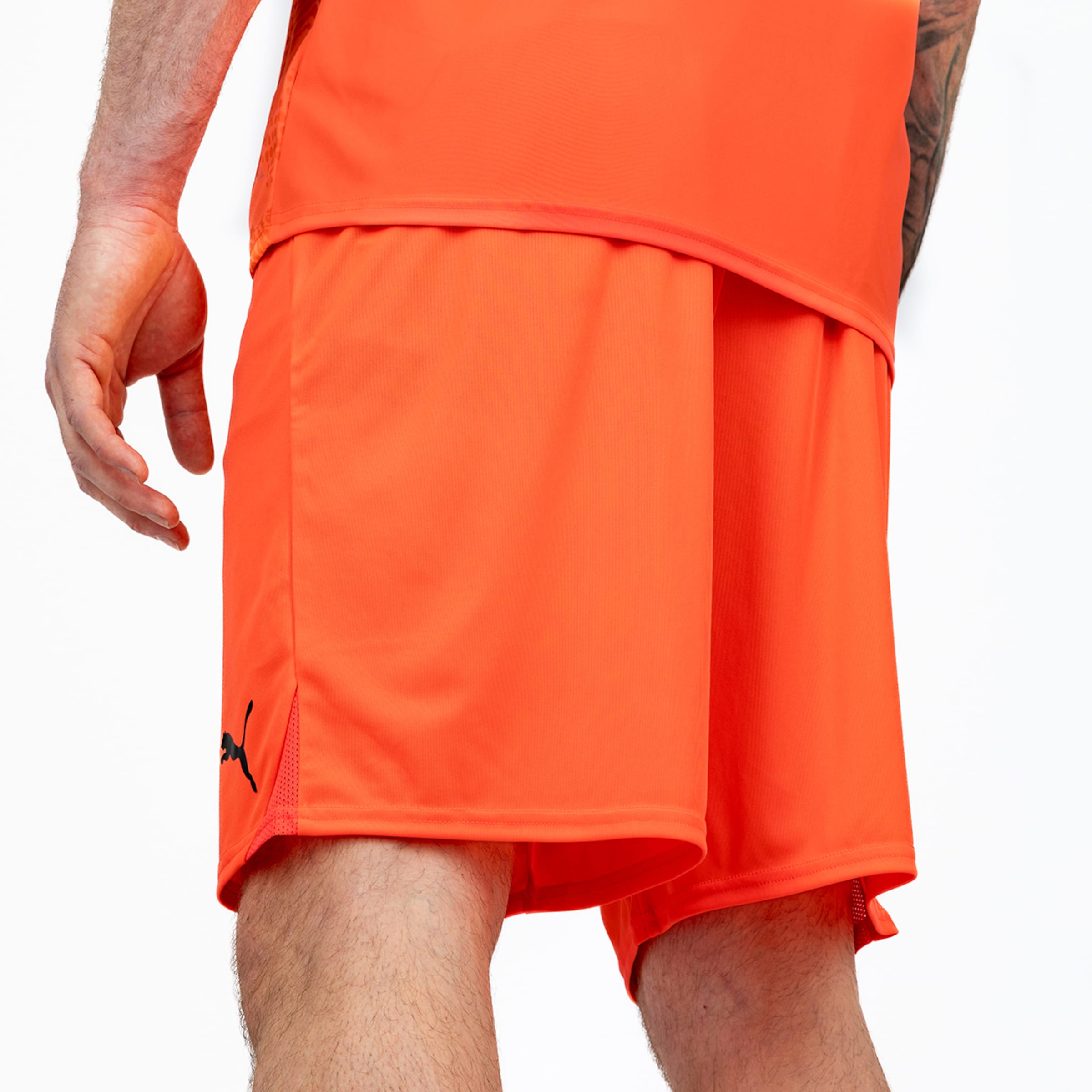 Rückansicht einer Person in leuchtend orangefarbenen Puma-Sportshorts mit schwarzem Logo vor weißem Hintergrund.