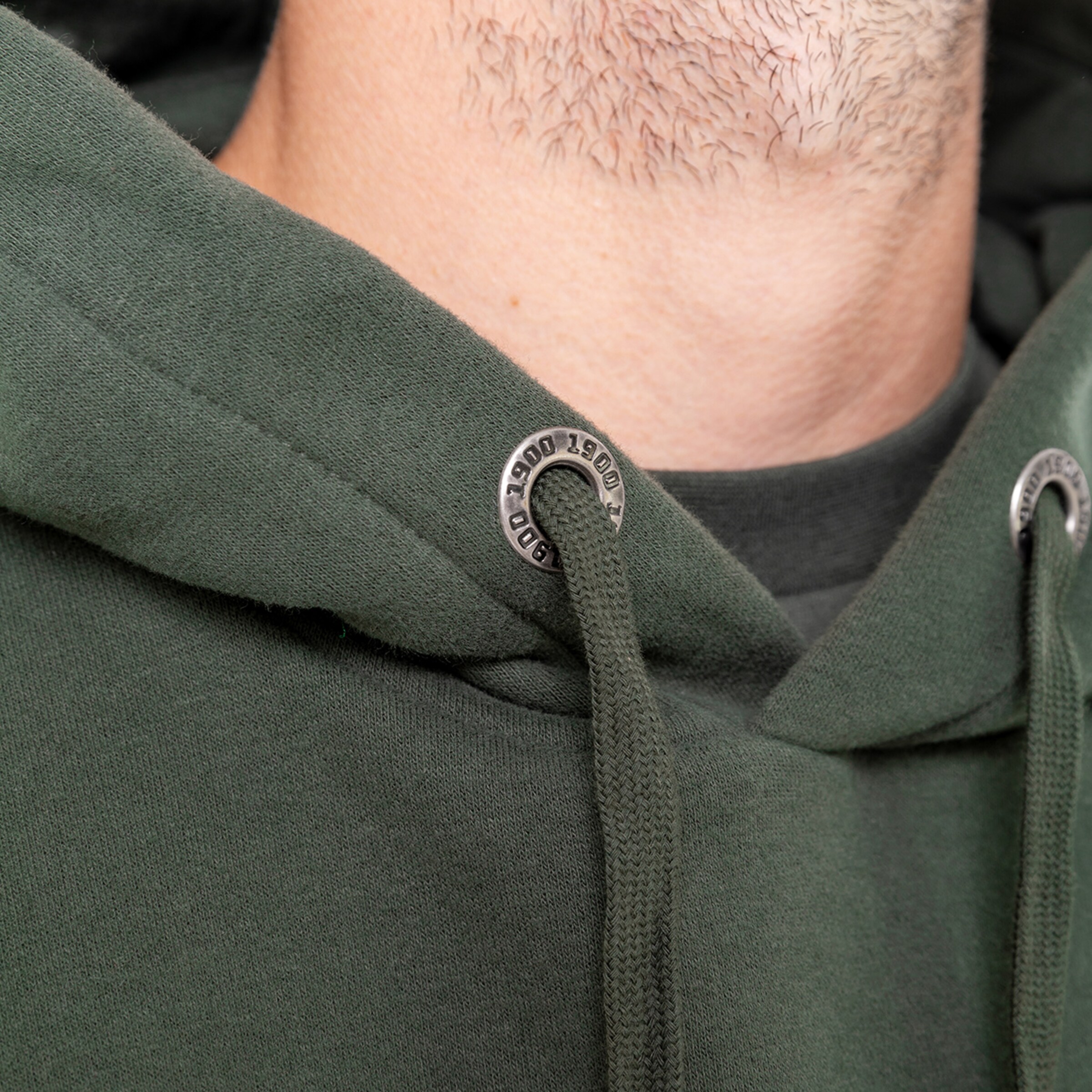 Nahaufnahme eines grünen Hoodies mit metallischen Details am Kragen.