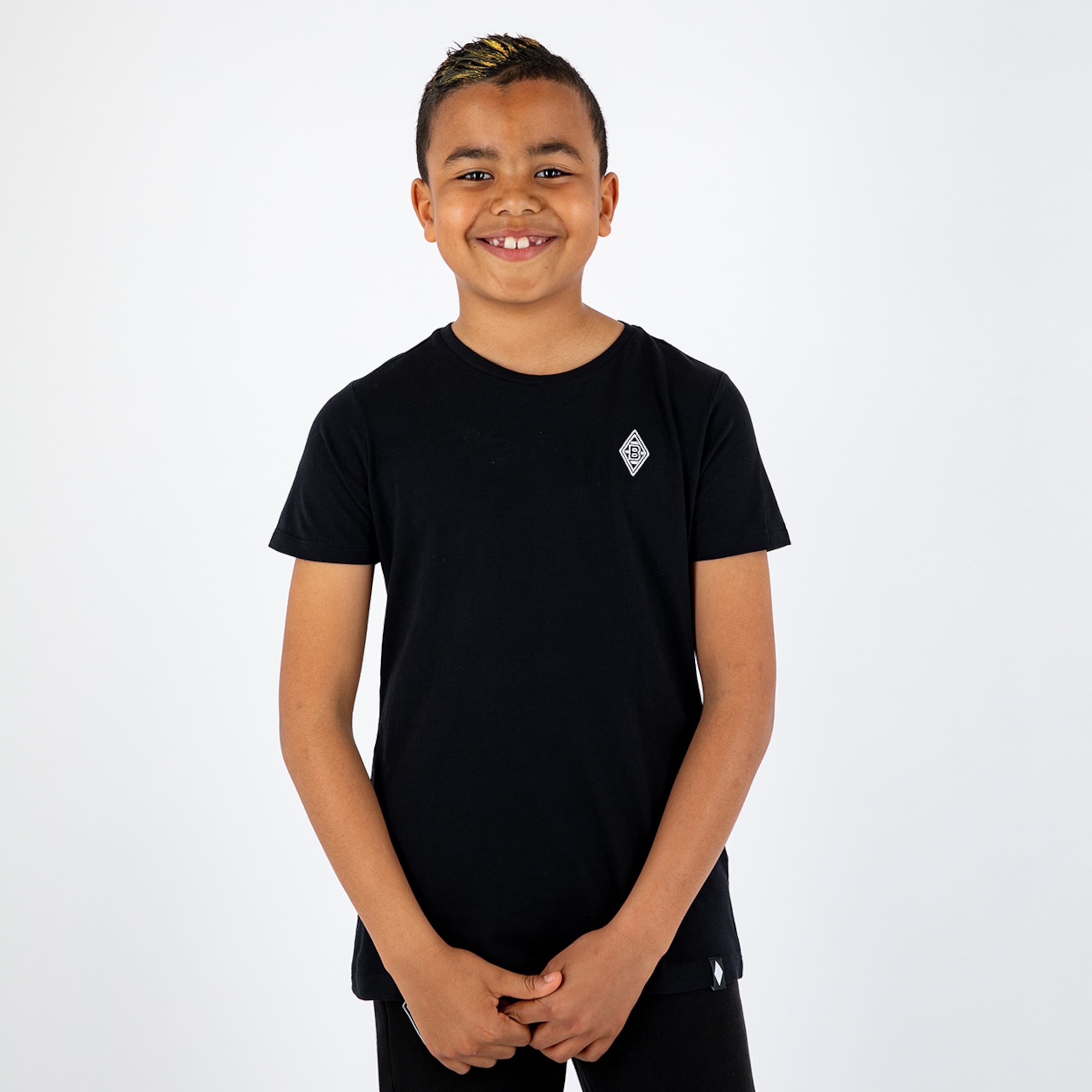 Junge in schwarz kurzem T-Shirt mit Borussia Mönchengladbach-Logo lächelt.