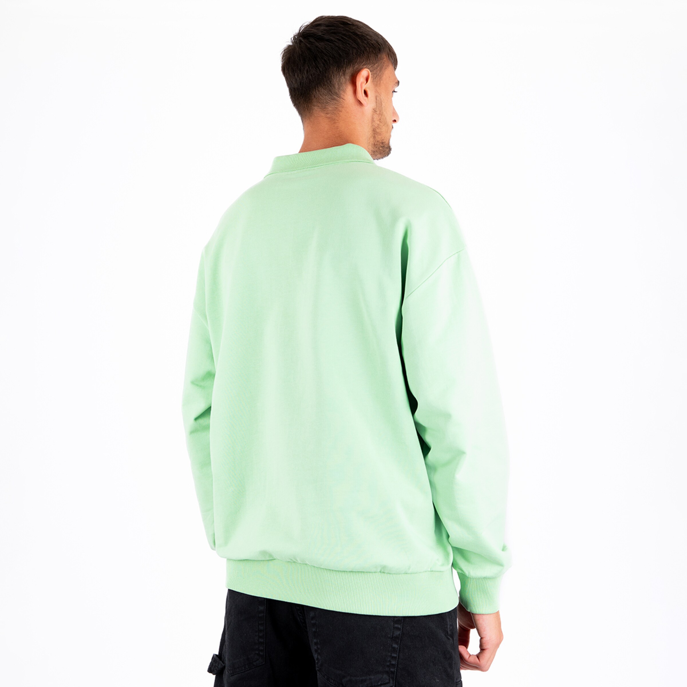 Man stands with his back to the camera wearing a mint green sweatshirt and black pants.
