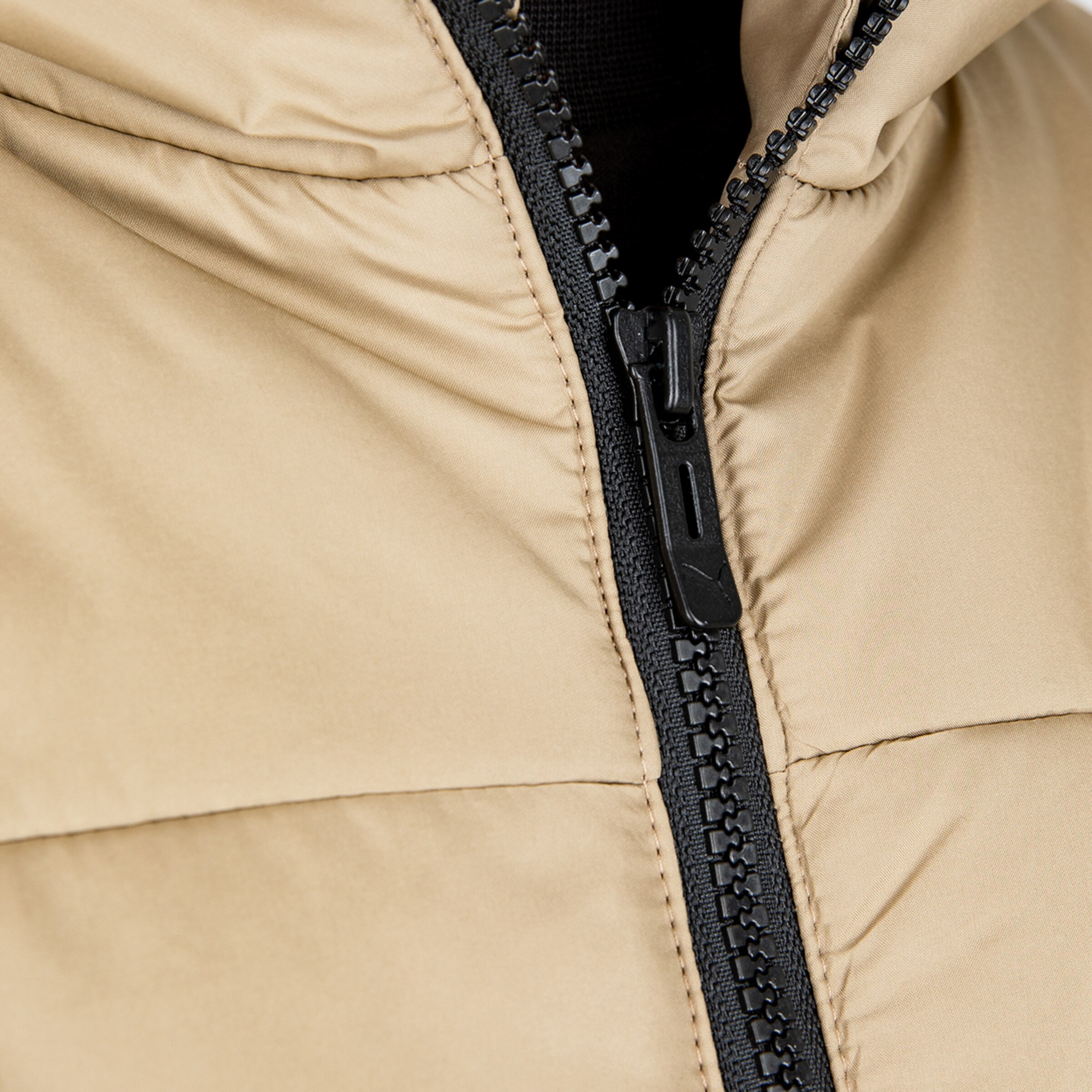 Nahaufnahme eines beigen Jackets mit schwarzem Reißverschluss.
