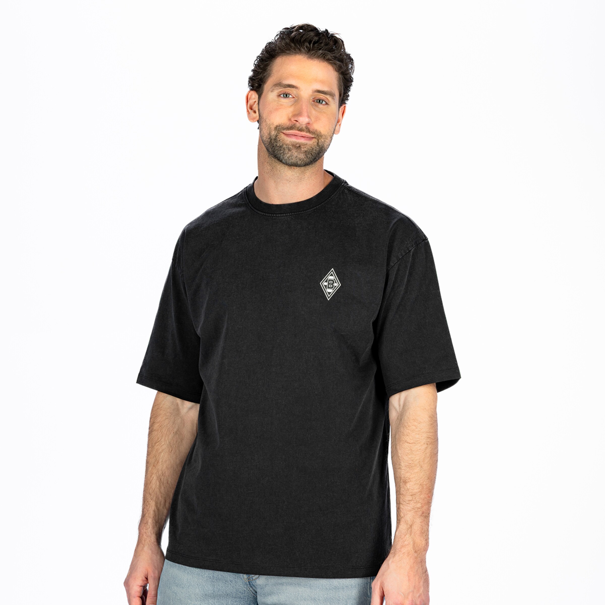 Man wearing a dark grey oversized t-shirt with a small chest logo, standing against a plain white background.