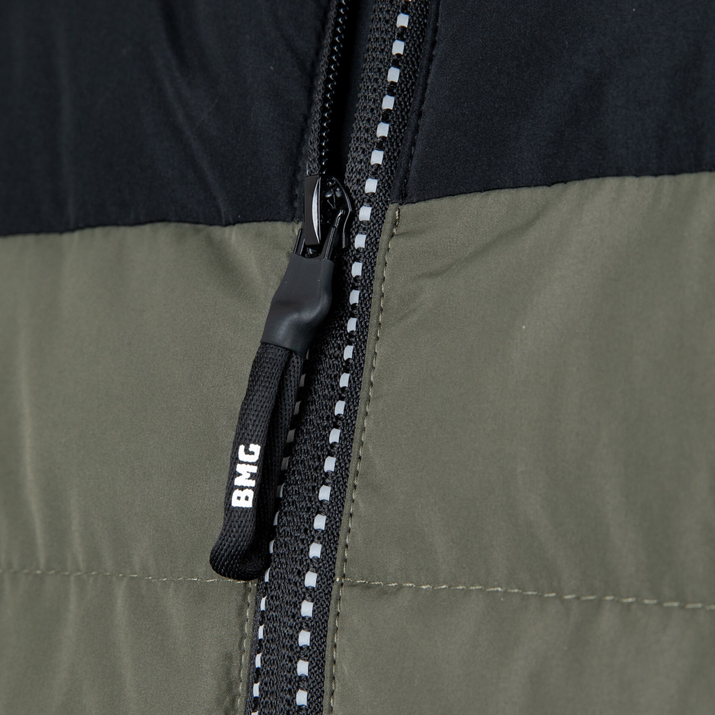 Details des Reißverschlusses einer Jacke in Olive und Schwarz mit BHG-Logo.