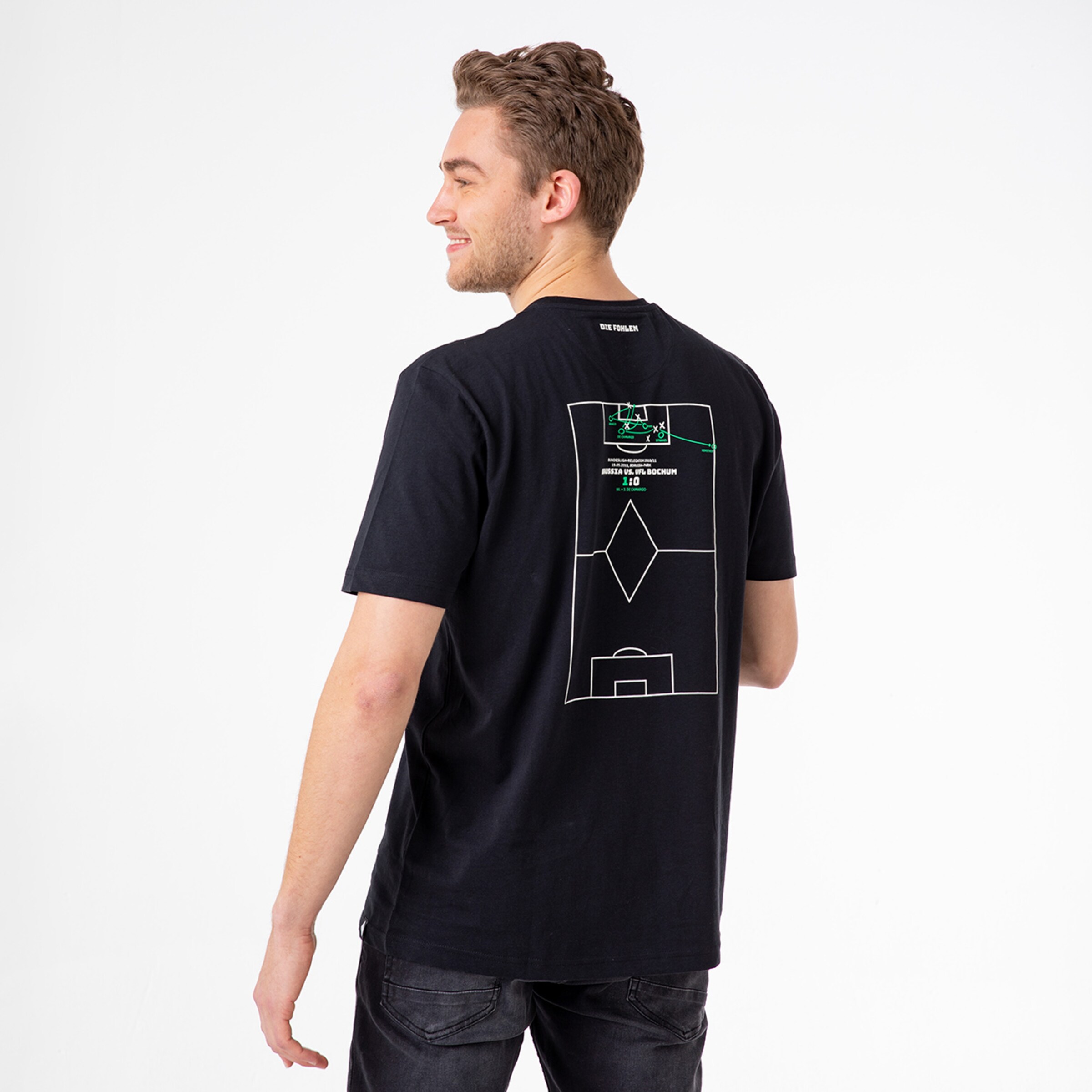 A man is wearing a black T-shirt featuring a graphic design on the back depicting a soccer field.