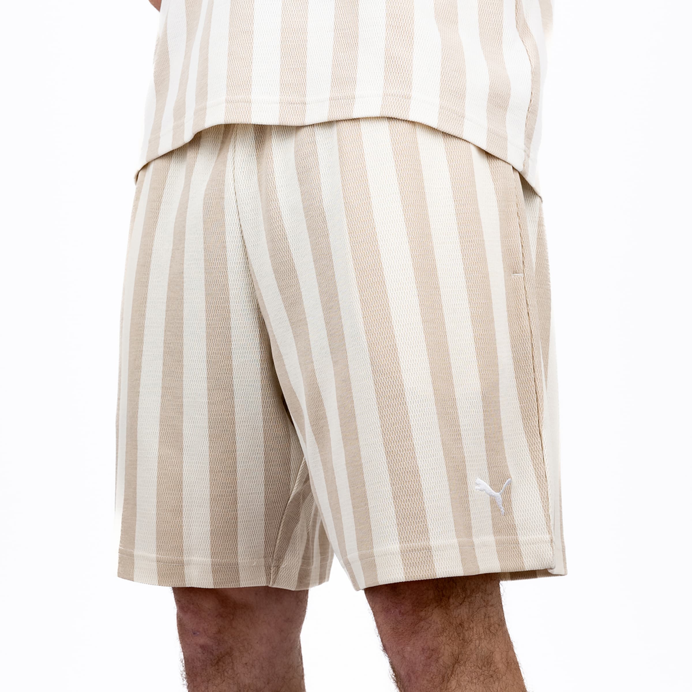 Person trägt beige-weiß vertikal gestreifte Mesh-Shorts und passendes Shirt. Auf dem linken Hosenbein ist ein weißes Puma-Logo.