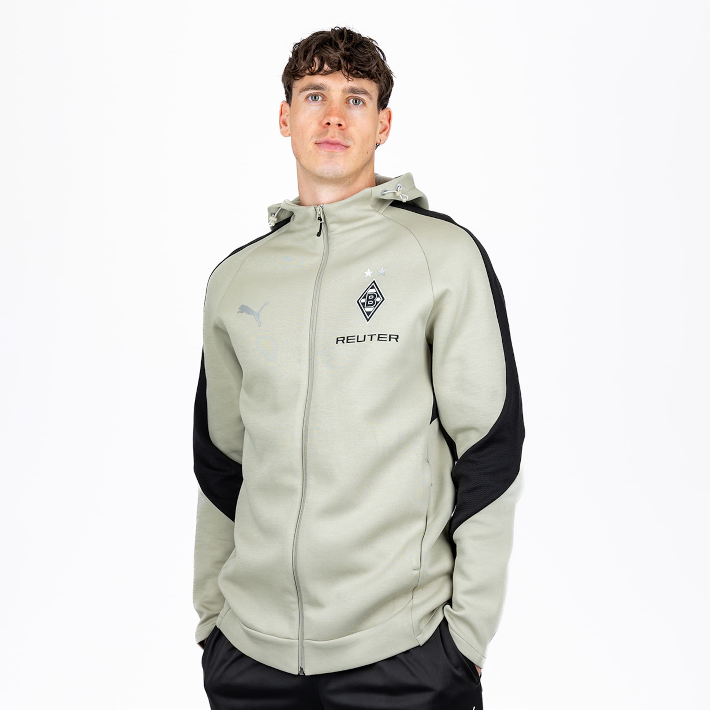 Mann in hellgrauem Full-Zip-Kapuzenpullover mit schwarzen Akzenten, Puma- und Borussia Mönchengladbach-Logo, sowie REUTER-Schriftzug, dazu schwarze Hose, vor weißem Hintergrund.