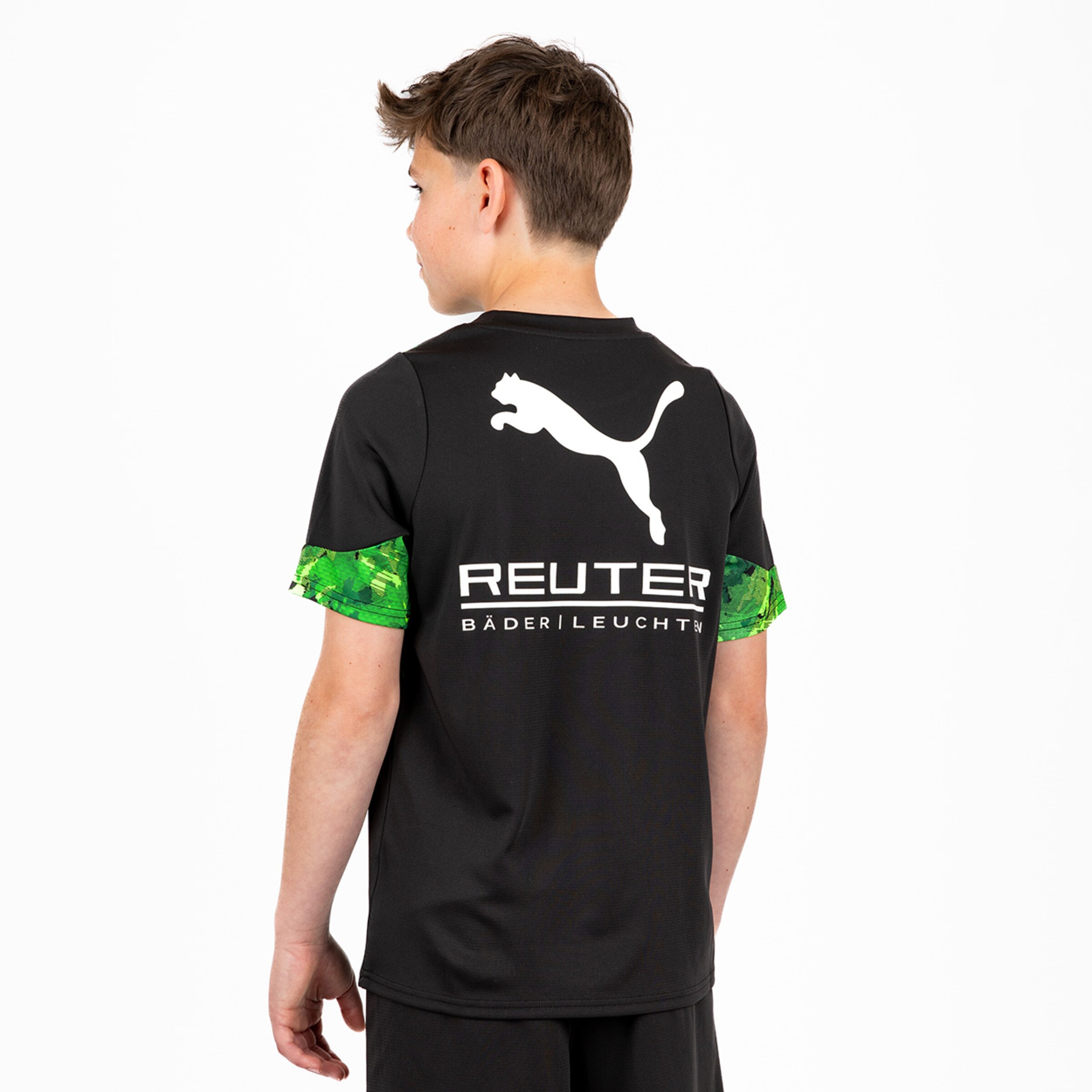Junge von hinten in schwarzem Puma-Trikot mit weißem Logo, REUTER-Sponsorenaufdruck und grün gemusterten Ärmeln.
