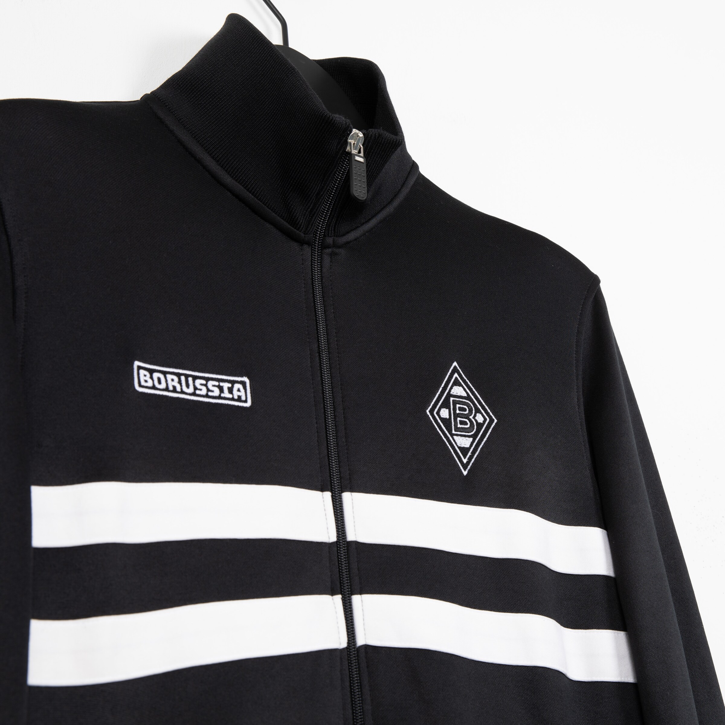 Schwarze Trainingsjacke von Borussia Mönchengladbach mit weißen Streifen und Logo.