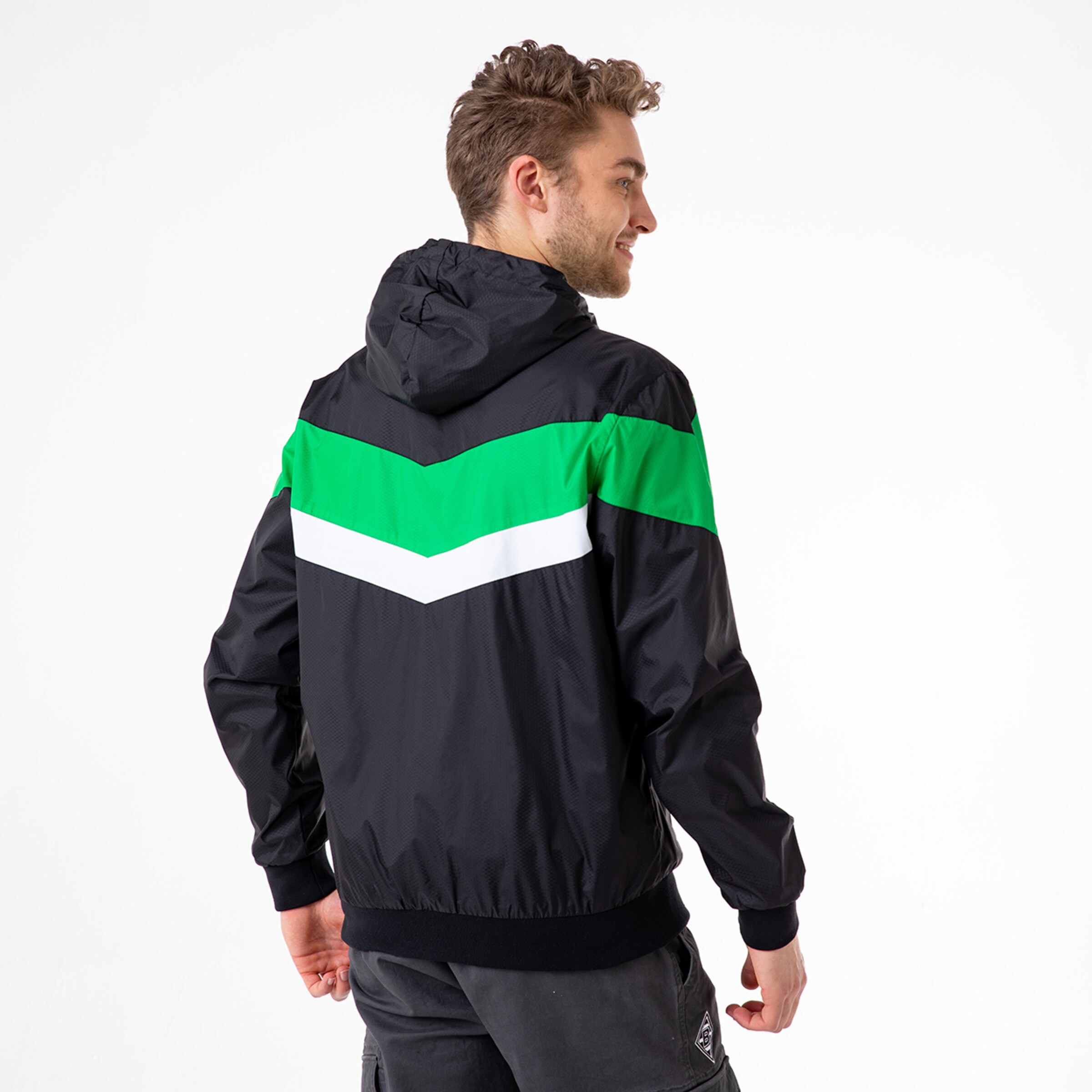 Mann trägt eine schwarze Windjacke mit grünen und weißen Streifen auf der Rückseite.