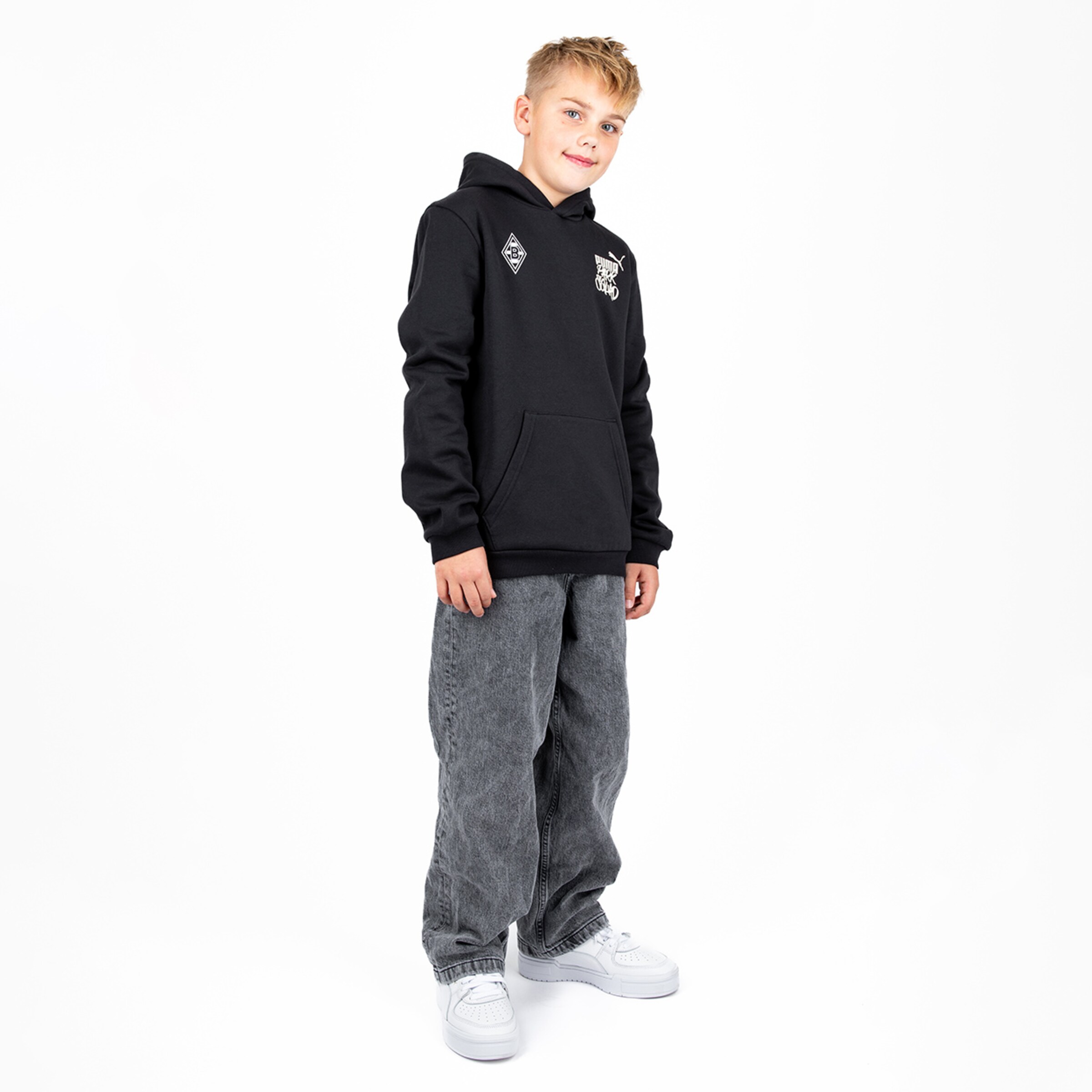 Young boy wearing a black hoodie and gray baggy jeans.