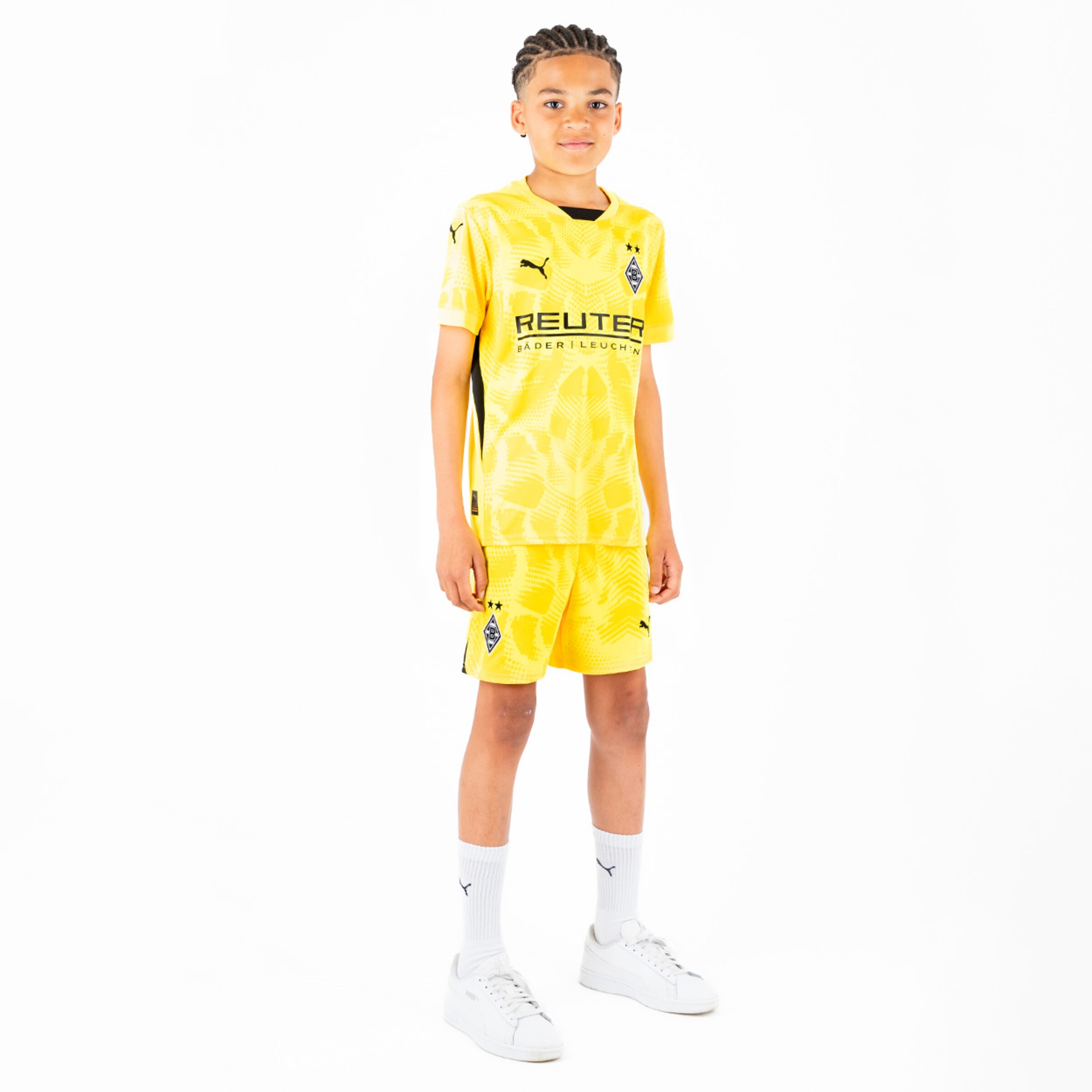Ein Junge trägt das gelbe Heimtrikot von Borussia Mönchengladbach mit passenden Shorts und weißen Sneakers.