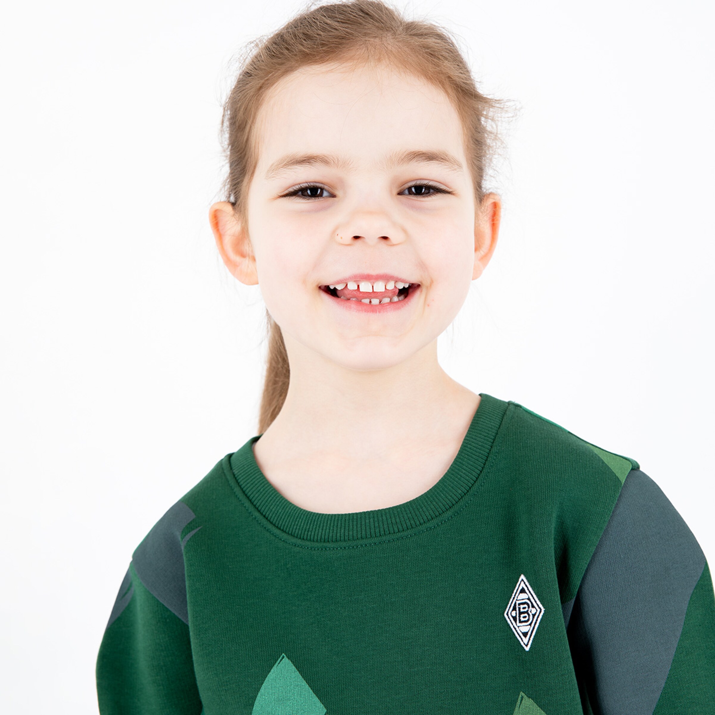Ein lächelndes Kind trägt einen grünen Pullover mit dem Borussia Mönchengladbach Logo.