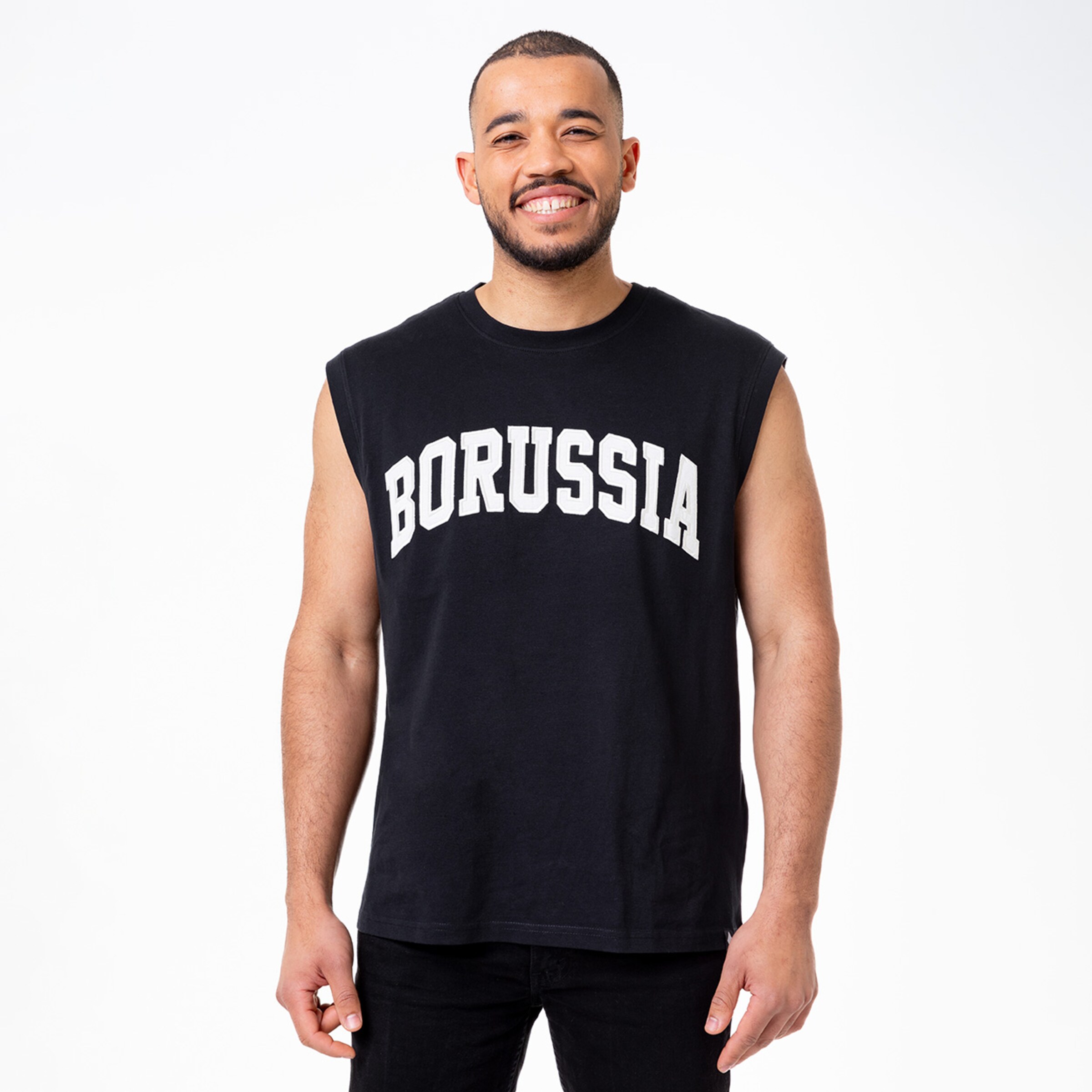 Ein lächelnder Mann trägt ein schwarzes ärmelloses T-Shirt mit der Aufschrift BORUSSIA.
