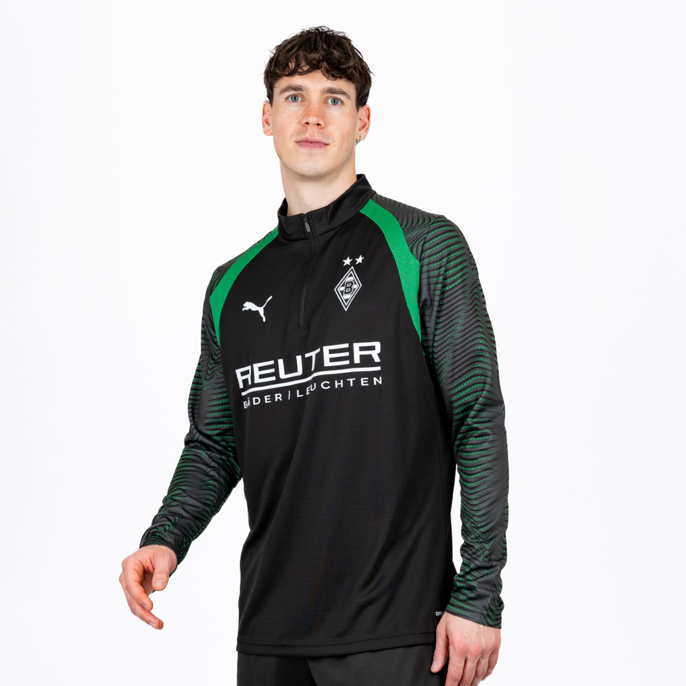 Mann in einem schwarz-grünen Borussia Mönchengladbach Trainings-Oberteil mit Viertelreißverschluss, strukturierten Ärmeln, Puma-Logo, Vereinswappen mit zwei Sternen und 'REUTER BÄDER/LEUCHTEN' Sponsor, vor weißem Hintergrund.